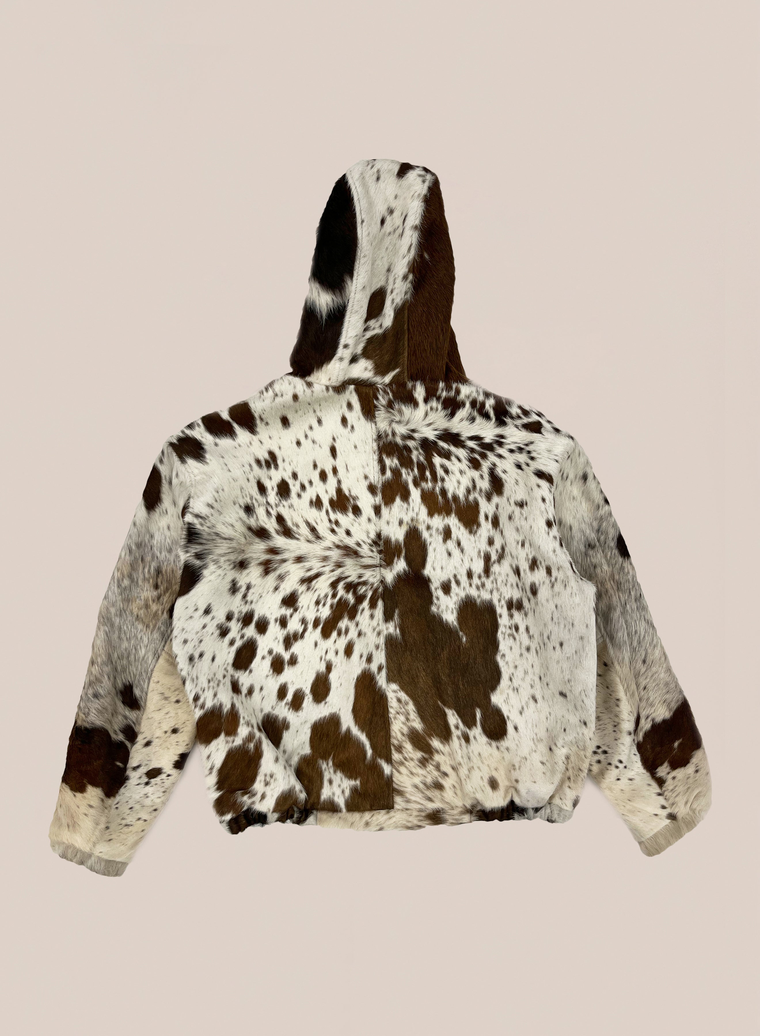 The FOUND Cowhide Drover Hoodie is a unique unisex outerwear piece made from brown and white spotted genuine cowhide, shown laid flat and photographed from the back against a plain background.