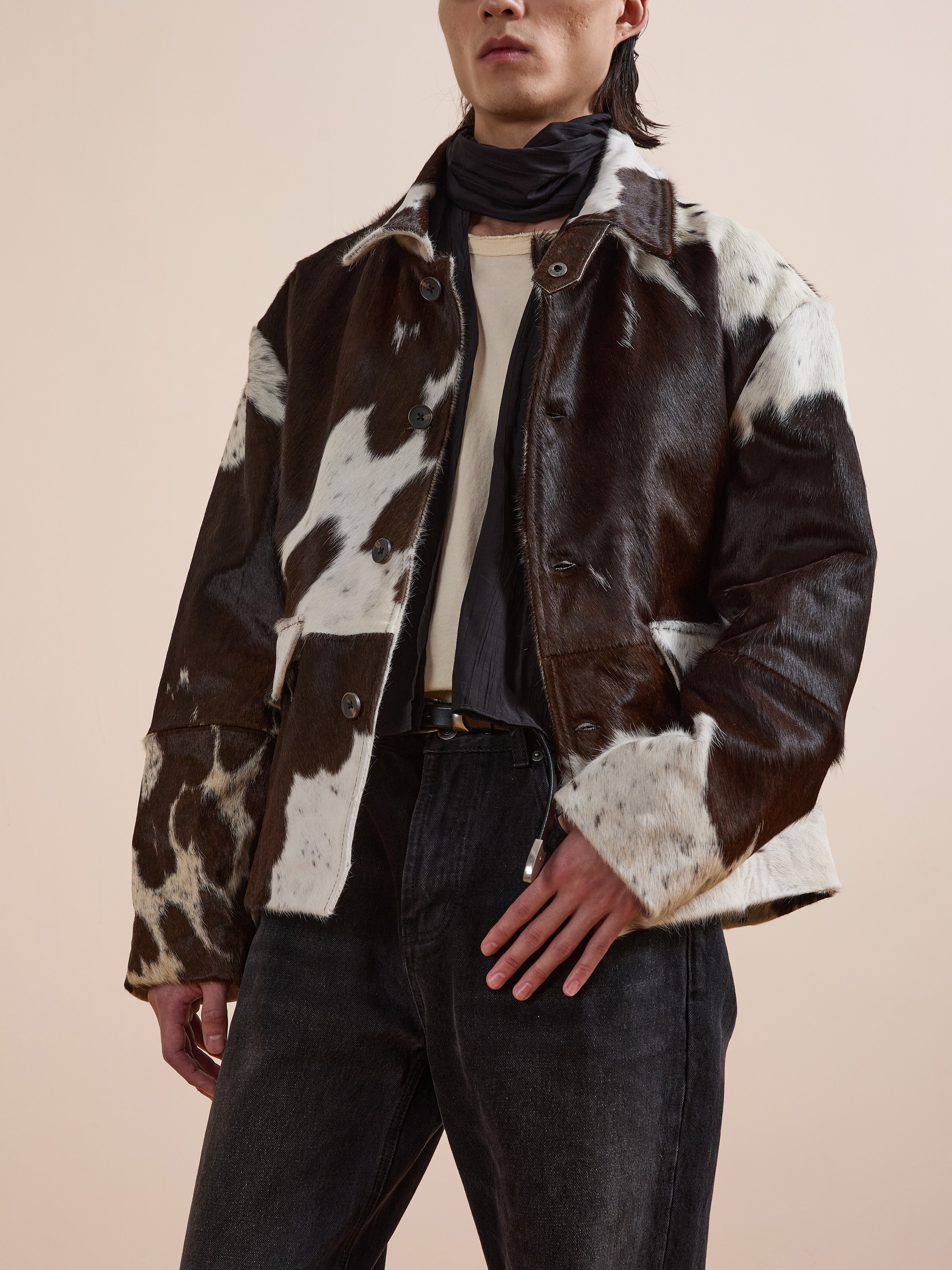 A person wearing the FOUND Cowhide Prairie Utility Jacket, paired with a cream shirt, dark jeans, and a black scarf, stands against a neutral background to showcase this standout piece.
