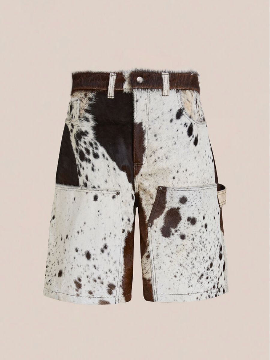 The Found Cowhide Prairie Carpenter Shorts feature a brown and white cow-print, front and side pockets, and a unisex relaxed fit, shown on a plain beige background.
