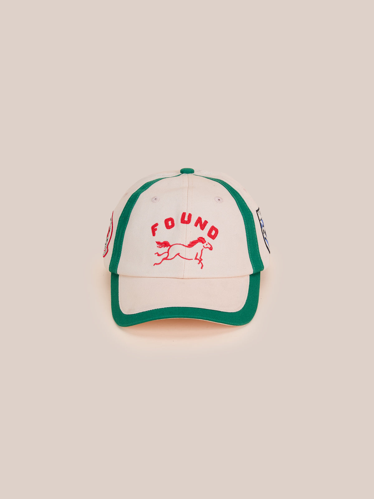 The Crestline Racing Cap by Found is a white and green equestrian cap with “FOUND” and a red running horse graphic for vintage club vibes.