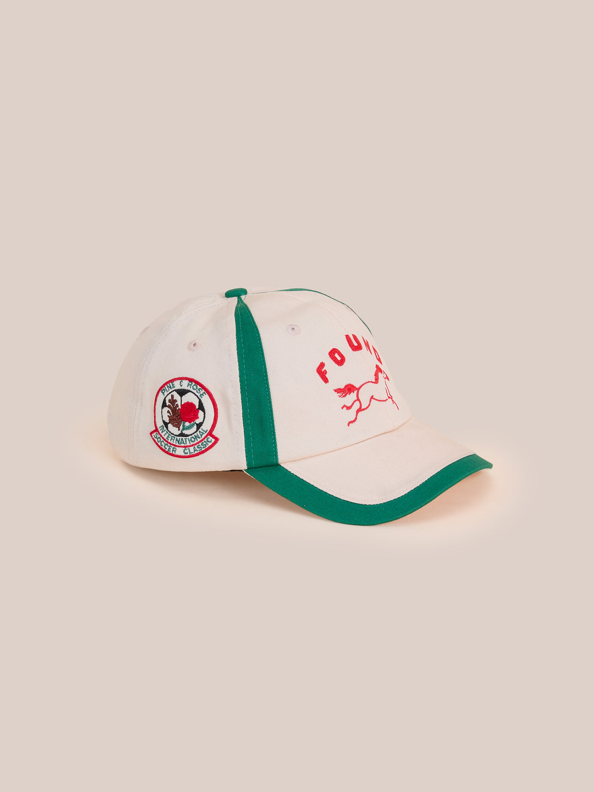 The Crestline Racing Cap by Found features beige with green trim, red “FOUND” text, a running animal graphic, and an embroidered side patch.