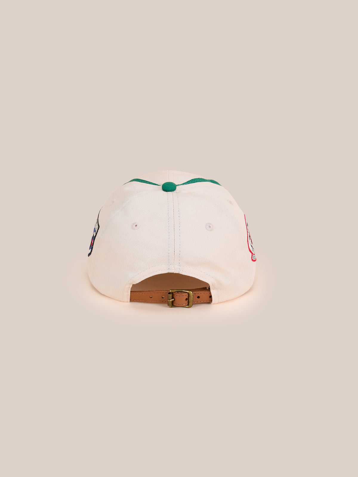 A beige Crestline Racing Cap by Found shown from the back, featuring a brown adjustable strap with metal buckle and a green top button.