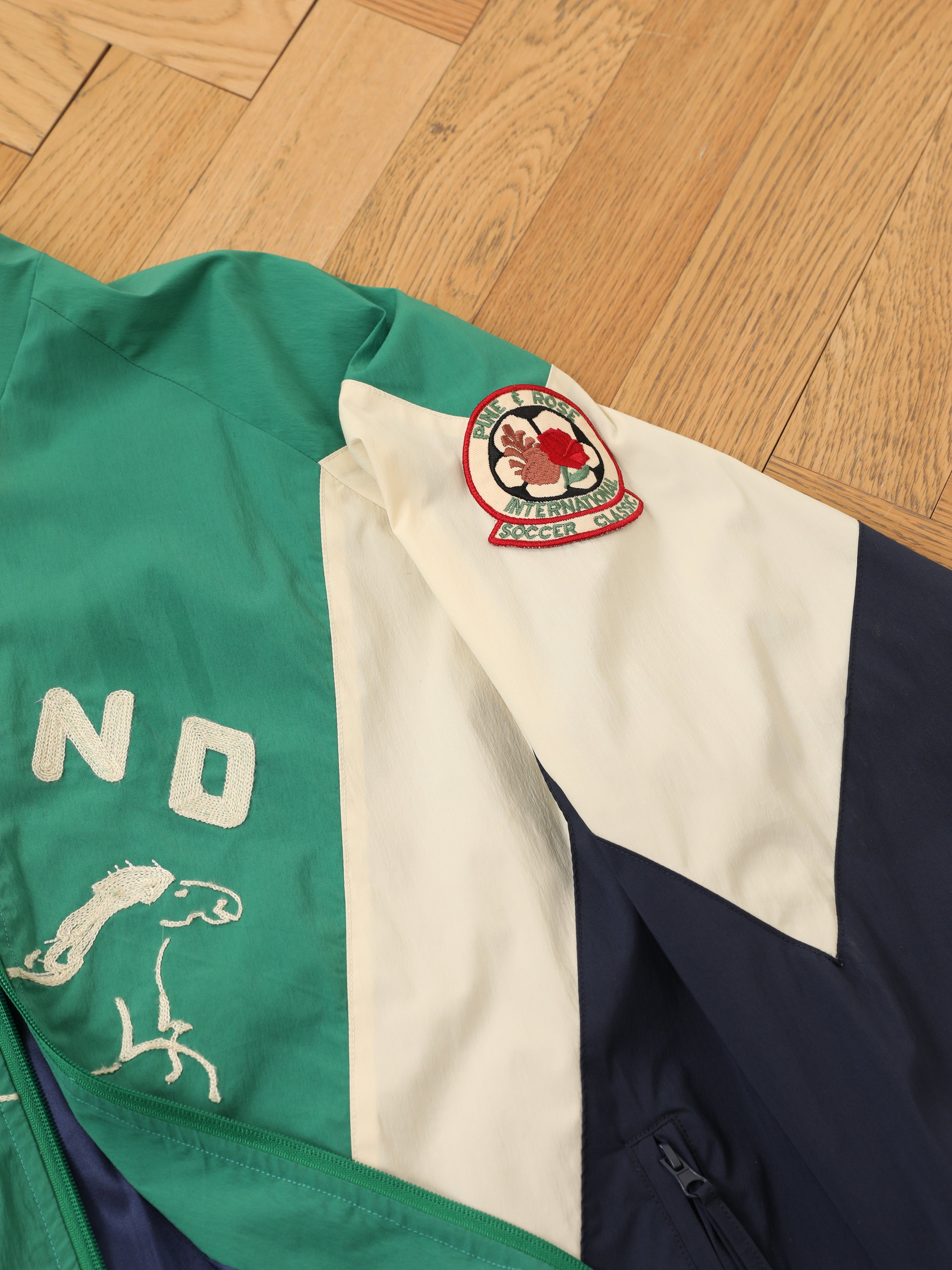 The FOUND Crestline Sport Zip Jacket is a lightweight windbreaker with green, white, and navy panels, a polar bear logo patch on the sleeve, and vintage sportswear-style embroidery on the back.