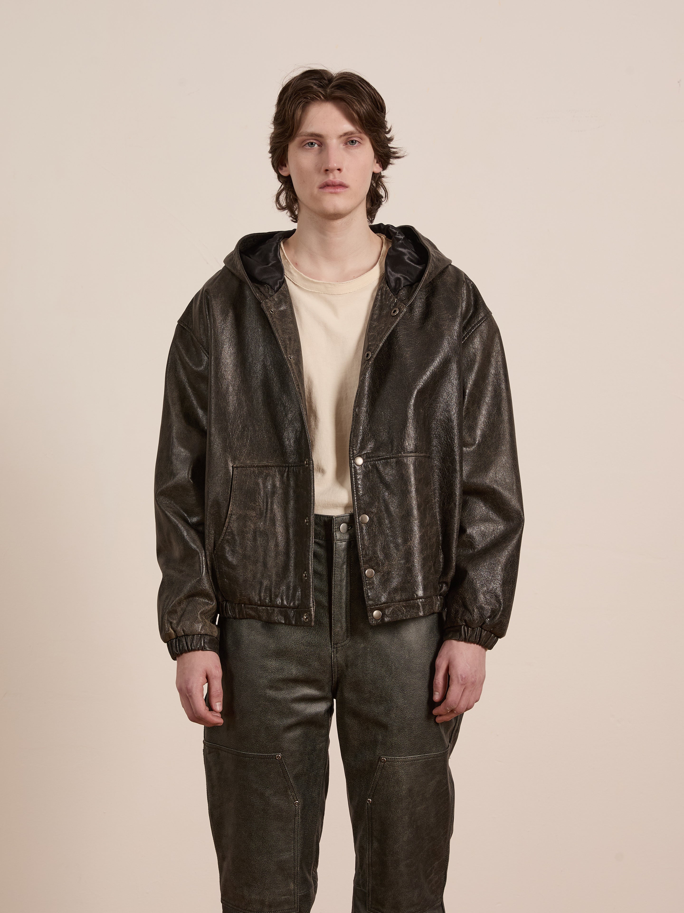 Dressed in a Distressed Genuine Leather Hoodie from Found over a light shirt, someone stands against a plain background, highlighting style and comfort.