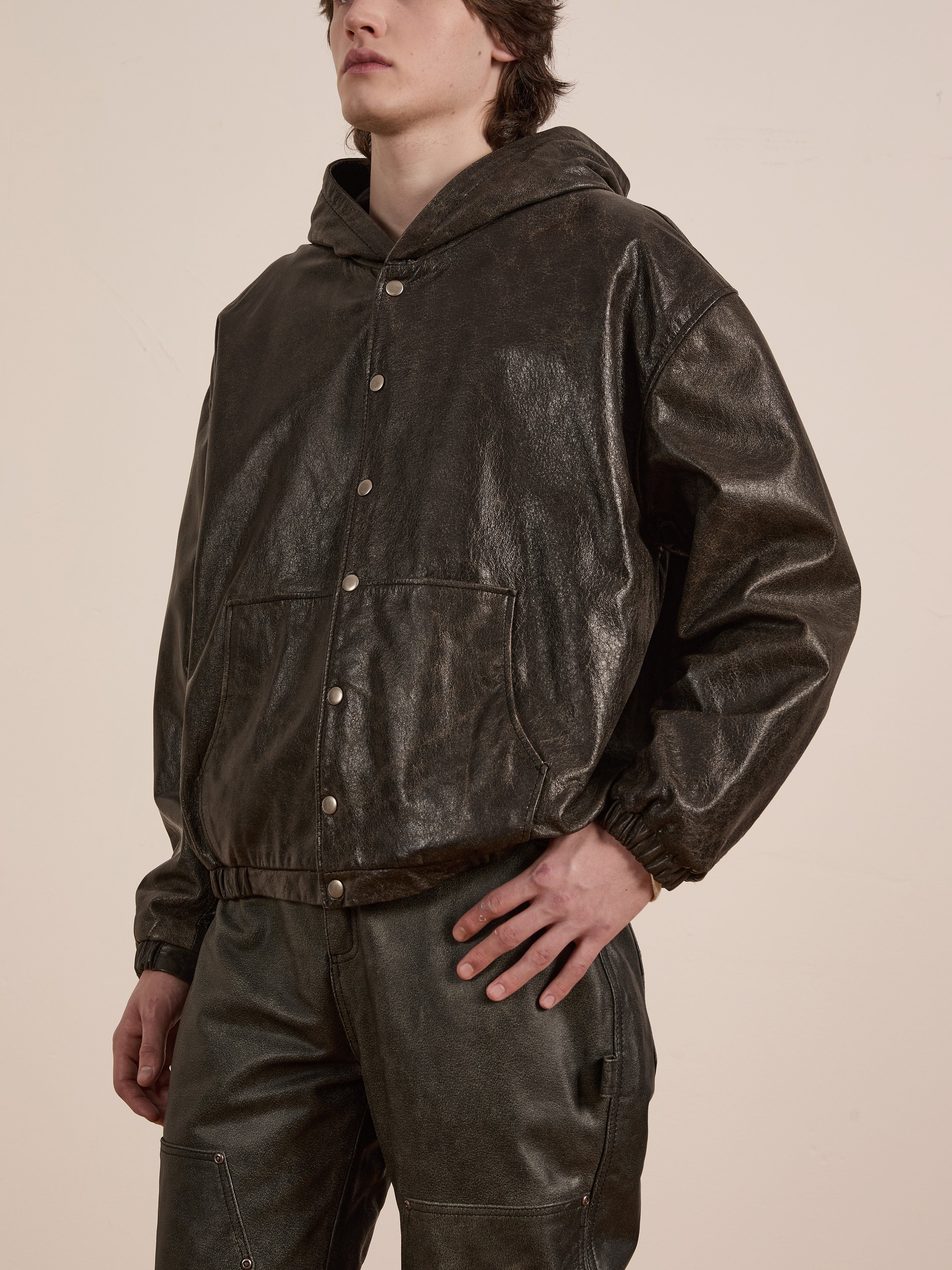 A person clad in Found's Distressed Genuine Leather Hoodie and matching pants stands with one hand on their hip.