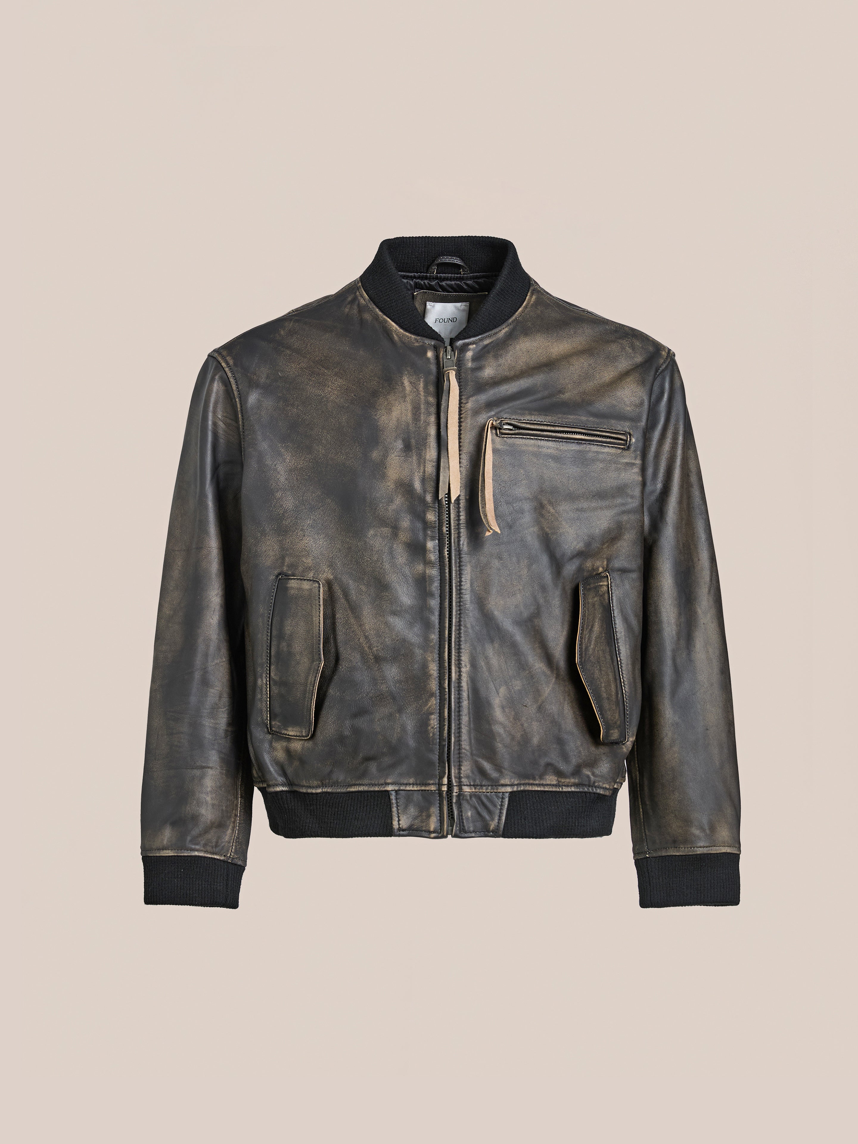 The Found Distressed Pavement Leather Bomber Jacket features a vintage-inspired design with a front zipper, chest pocket, and two waist pockets on a beige background.