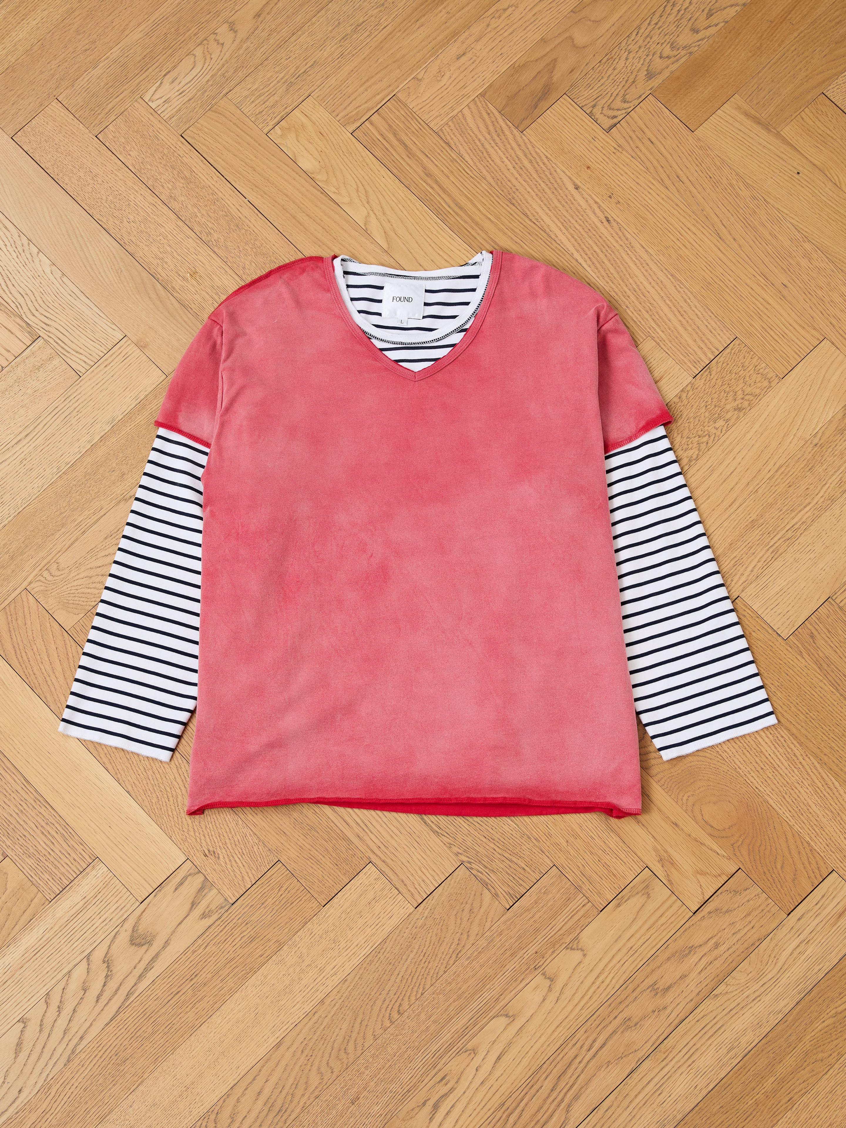 A pink sunfade wash V-neck shirt is layered over the FOUND Double Layer LS Tee in black and white stripes, laid flat on a wooden parquet floor.