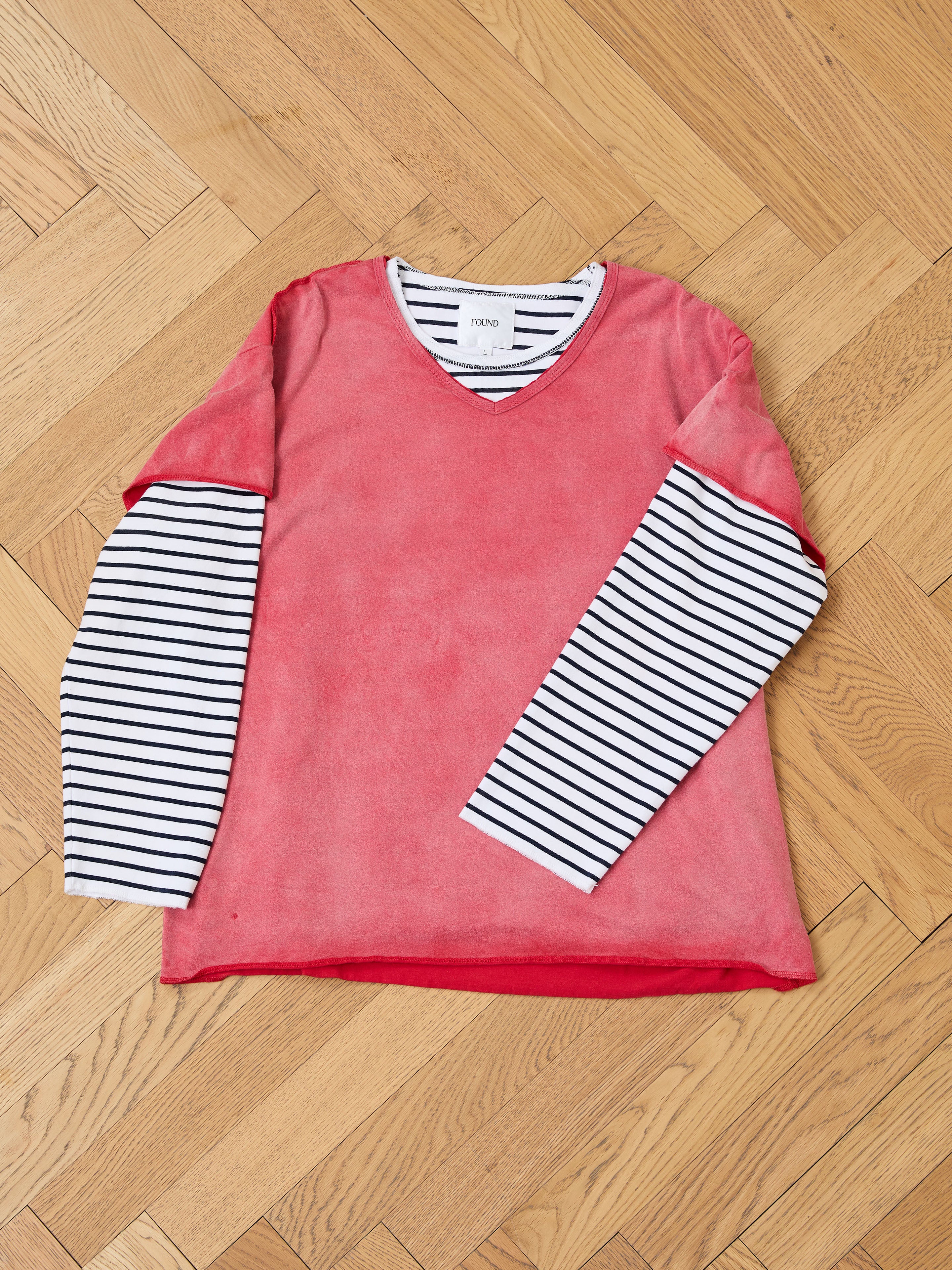 The FOUND Double Layer LS Tee features black and white stripes under a pink short-sleeve in a unisex relaxed fit, shown laid flat on a wooden herringbone floor.