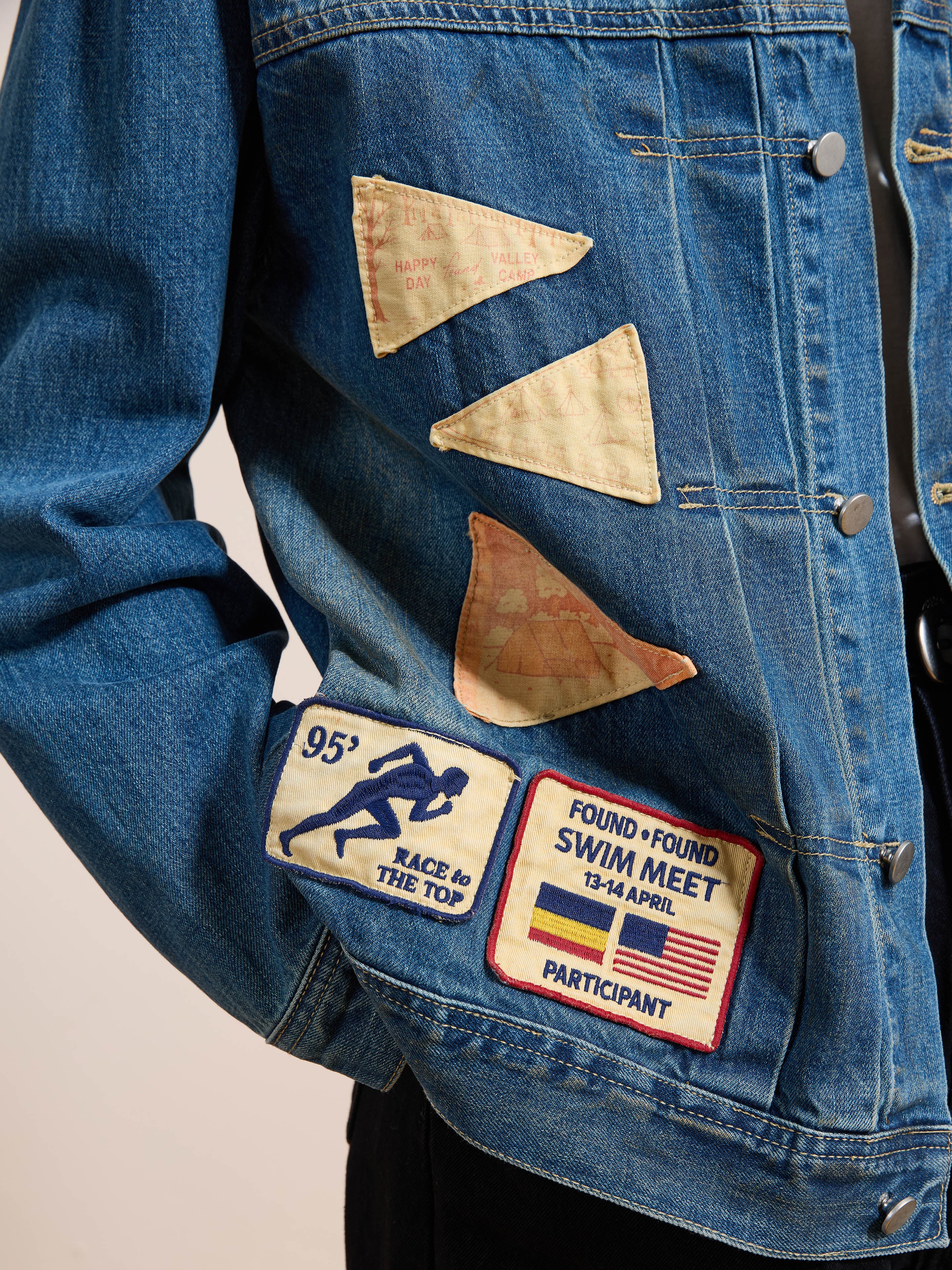 FOUND’s Denim Patchwork Jacket features three triangular fabric patches and two swim meet badges on the front, offering a vintage washed look and classic unisex relaxed fit.