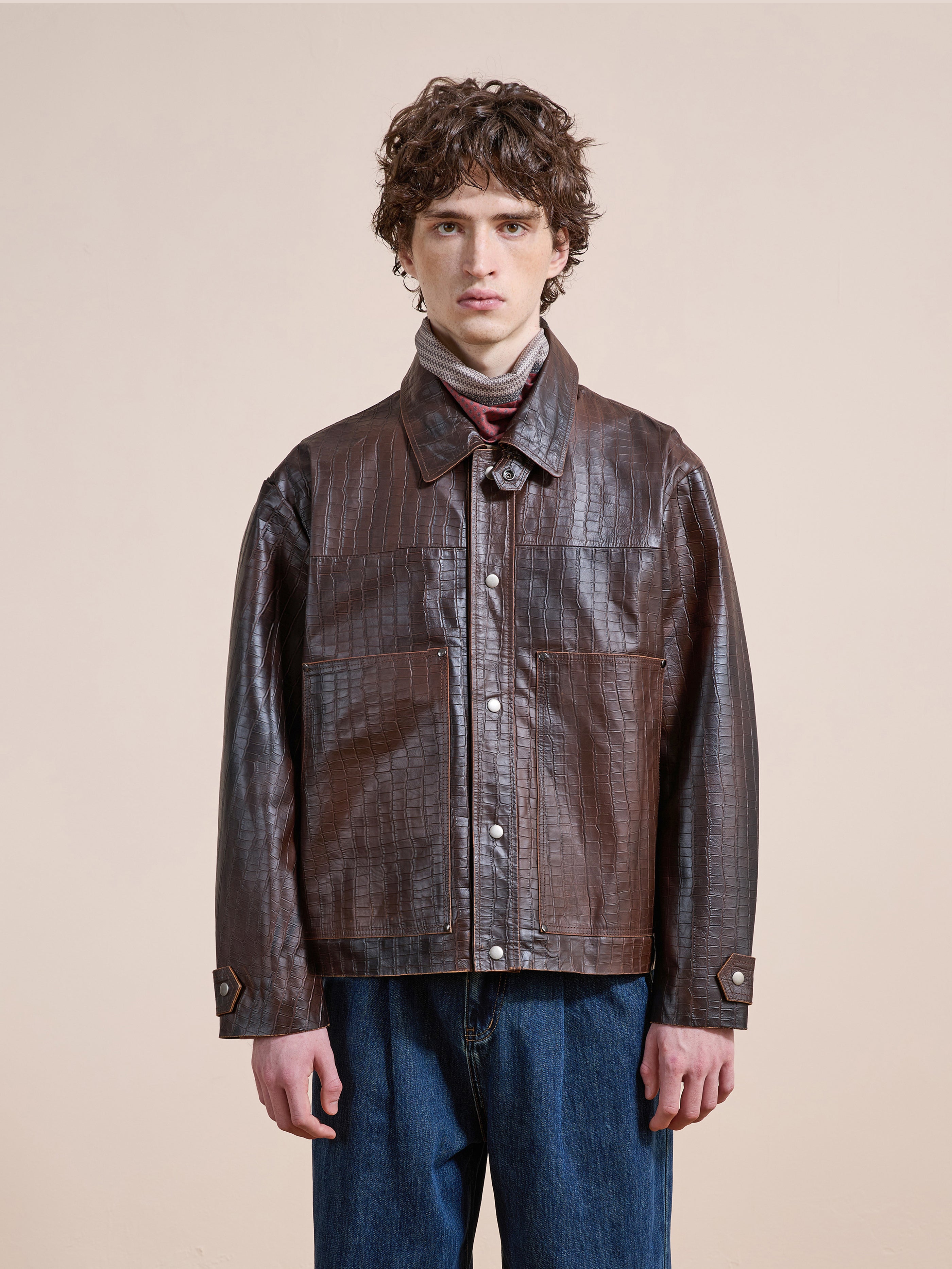 A person wears the FOUND Distressed Croc Embossed Leather Work Jacket over a turtleneck and blue jeans, standing facing forward against a plain beige background.