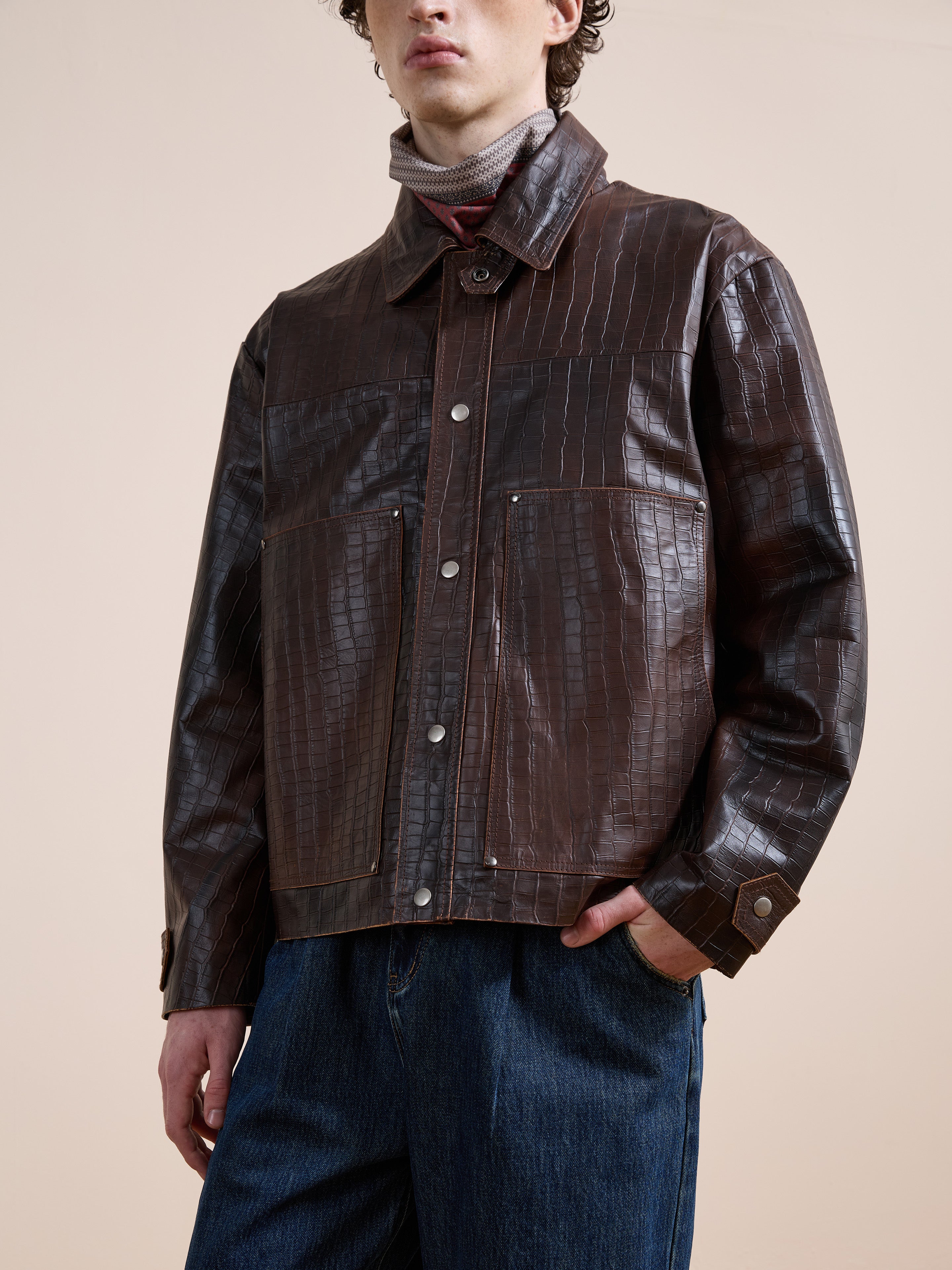 A person wearing the FOUND Distressed Croc Embossed Leather Work Jacket, a striped turtleneck, and blue jeans stands against a plain beige background.