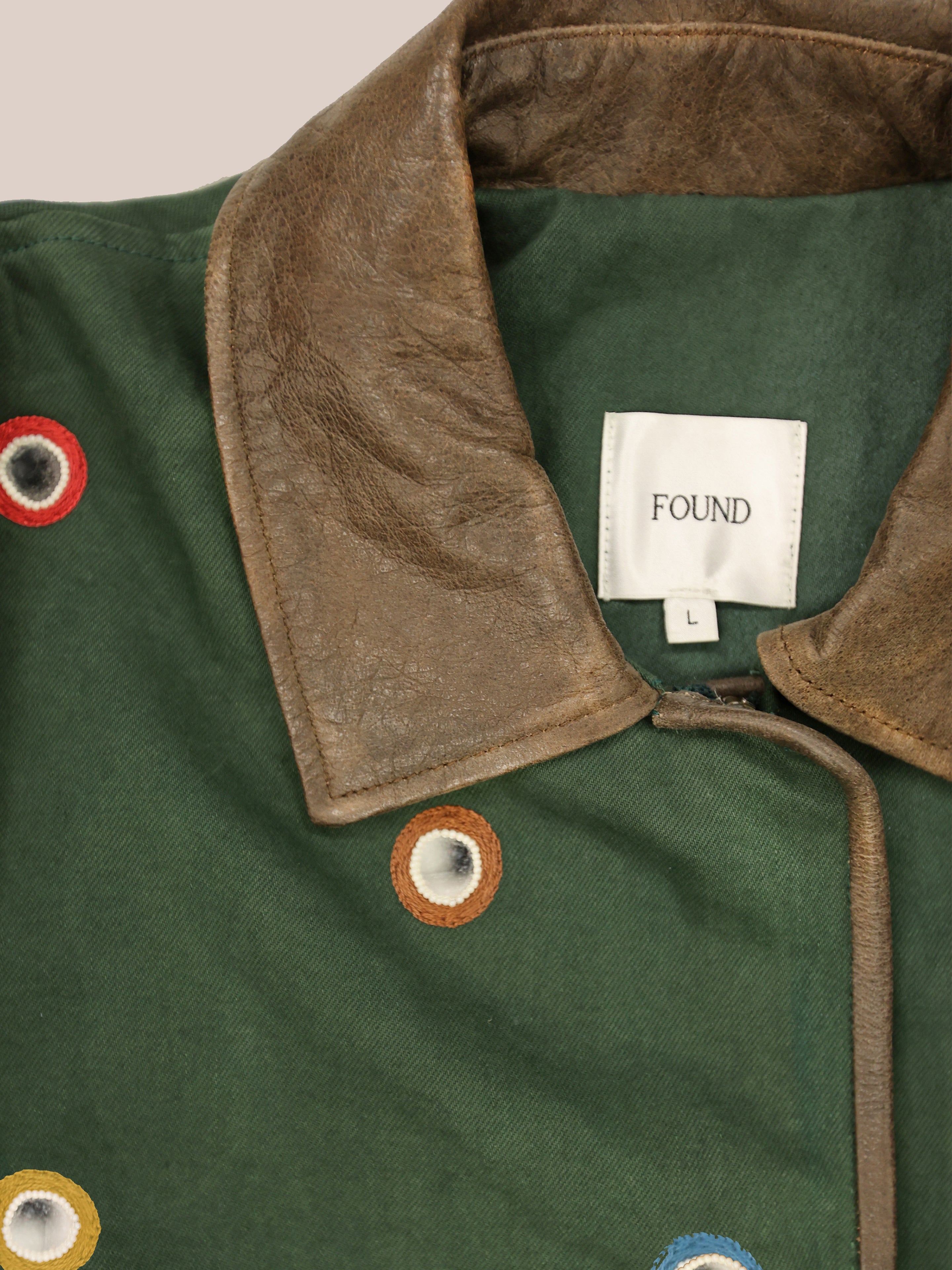 Hand Embroidered Mirror Abhala Jacket by Found features green cotton twill, a brown leather collar, multicolored stitched eyelets, and a white "FOUND L" label.