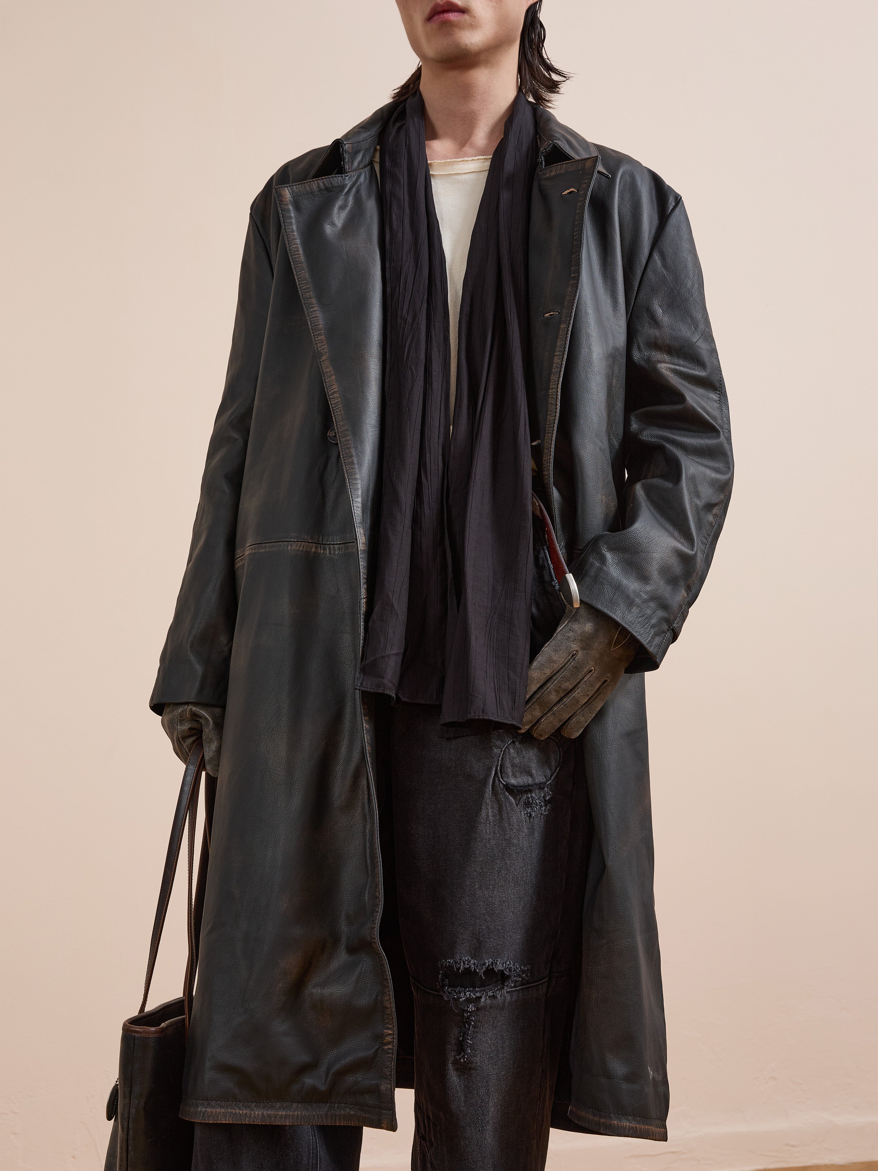 Model wears FOUND Distressed Leather Trench Coat with black scarf, gloves, white shirt, distressed jeans, and holds a black bag against a plain background.
