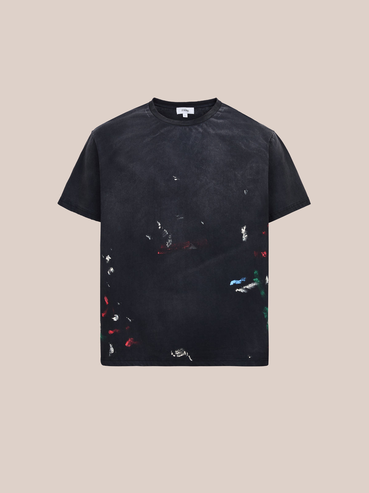 FOUND Distressed Paint Tee—A unisex, relaxed-fit black short-sleeve shirt featuring scattered red, blue, white, and green paint splatter details on a plain beige background.