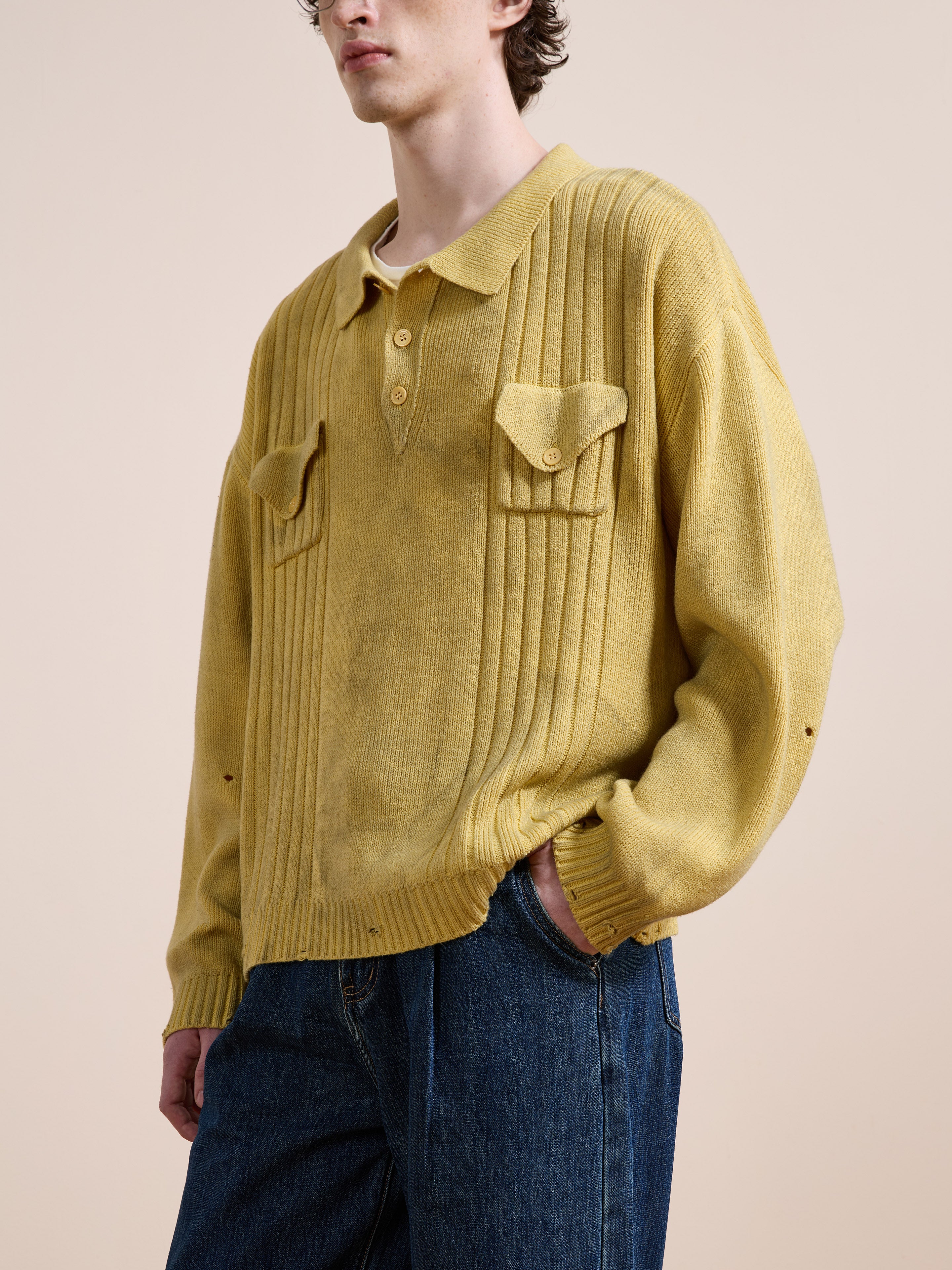 A person wears the FOUND Distressed Pullover Knit in yellow with chest pockets and blue jeans, standing against a plain beige background.