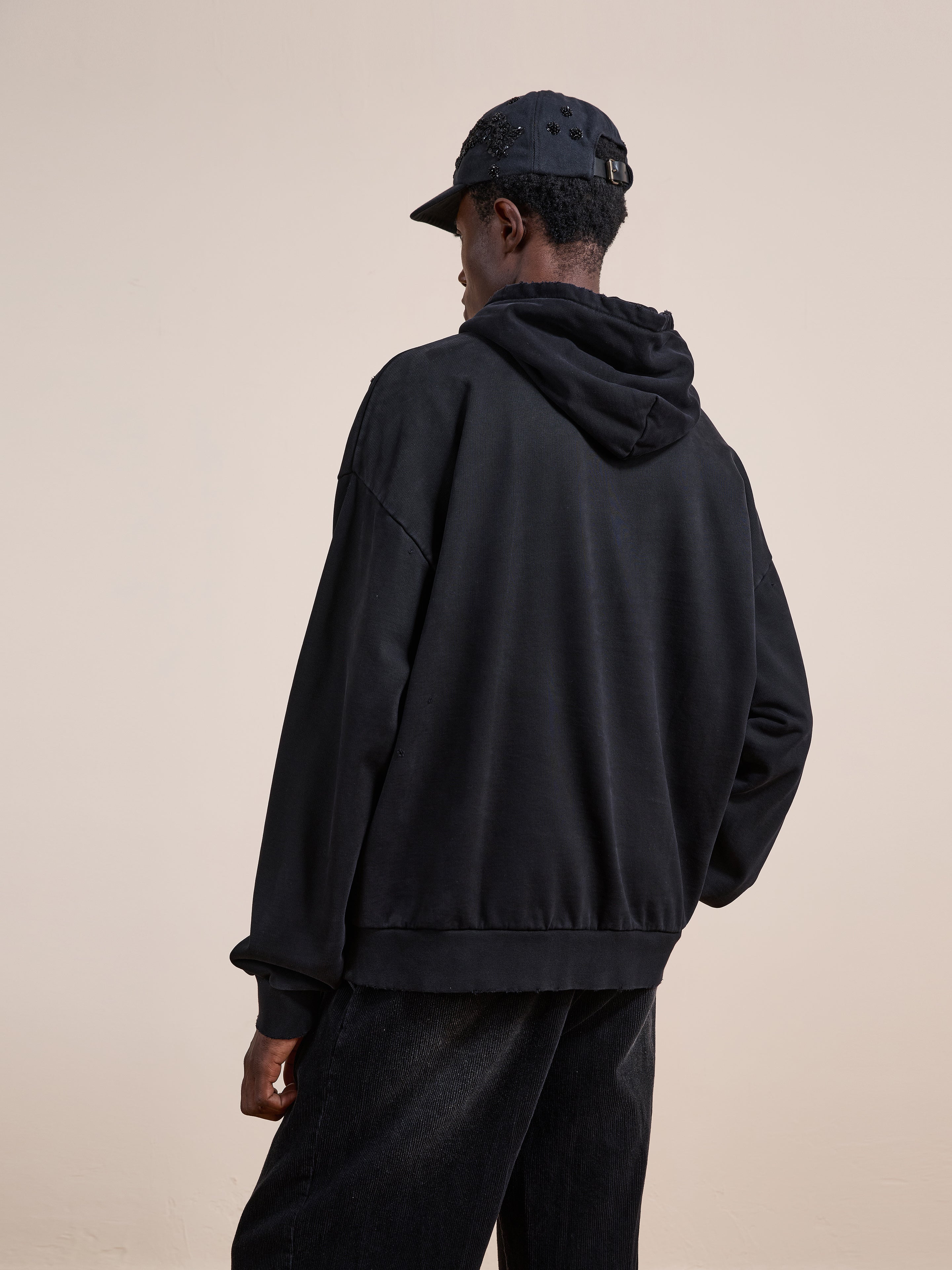 A person wearing the FOUND Distressed Pullover Hoodie stands facing away from the camera against a plain, light background.