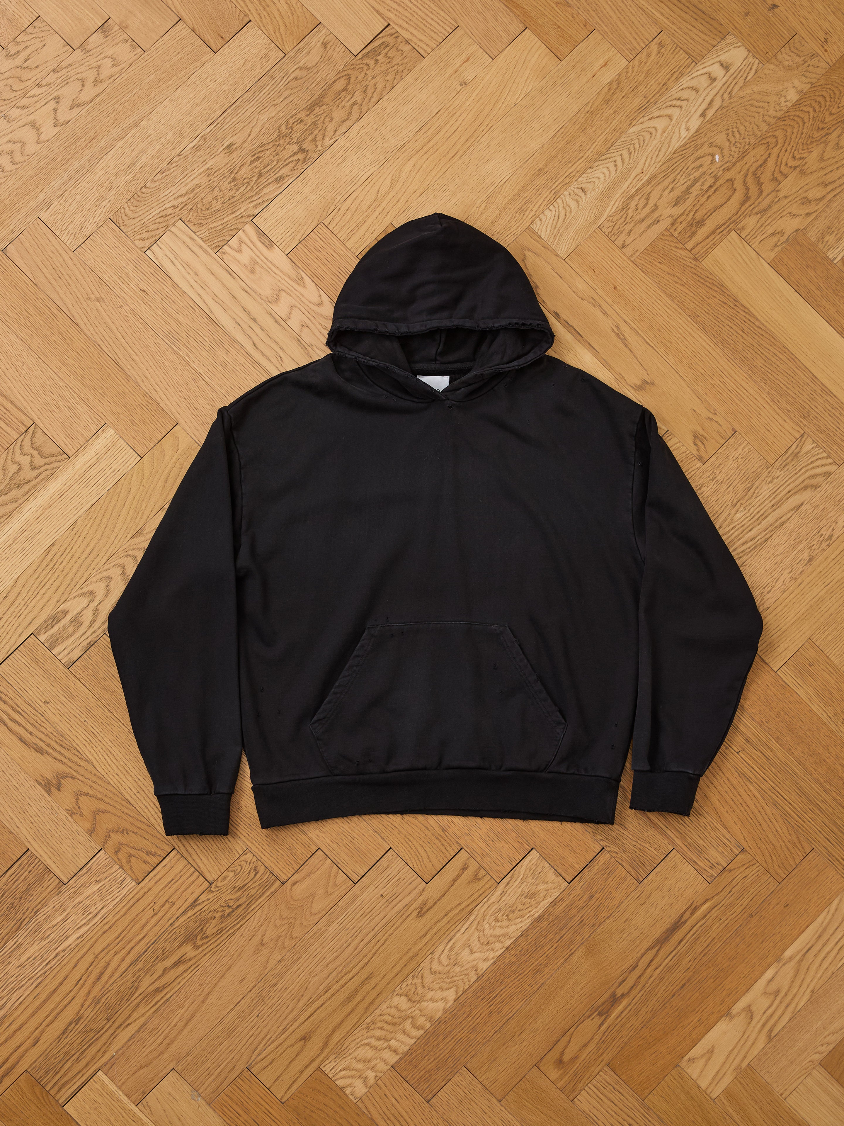 The FOUND Distressed Pullover Hoodie, featuring a front pocket and classic unisex relaxed fit, is displayed flat on a wooden parquet floor, highlighting its timeless vintage style.