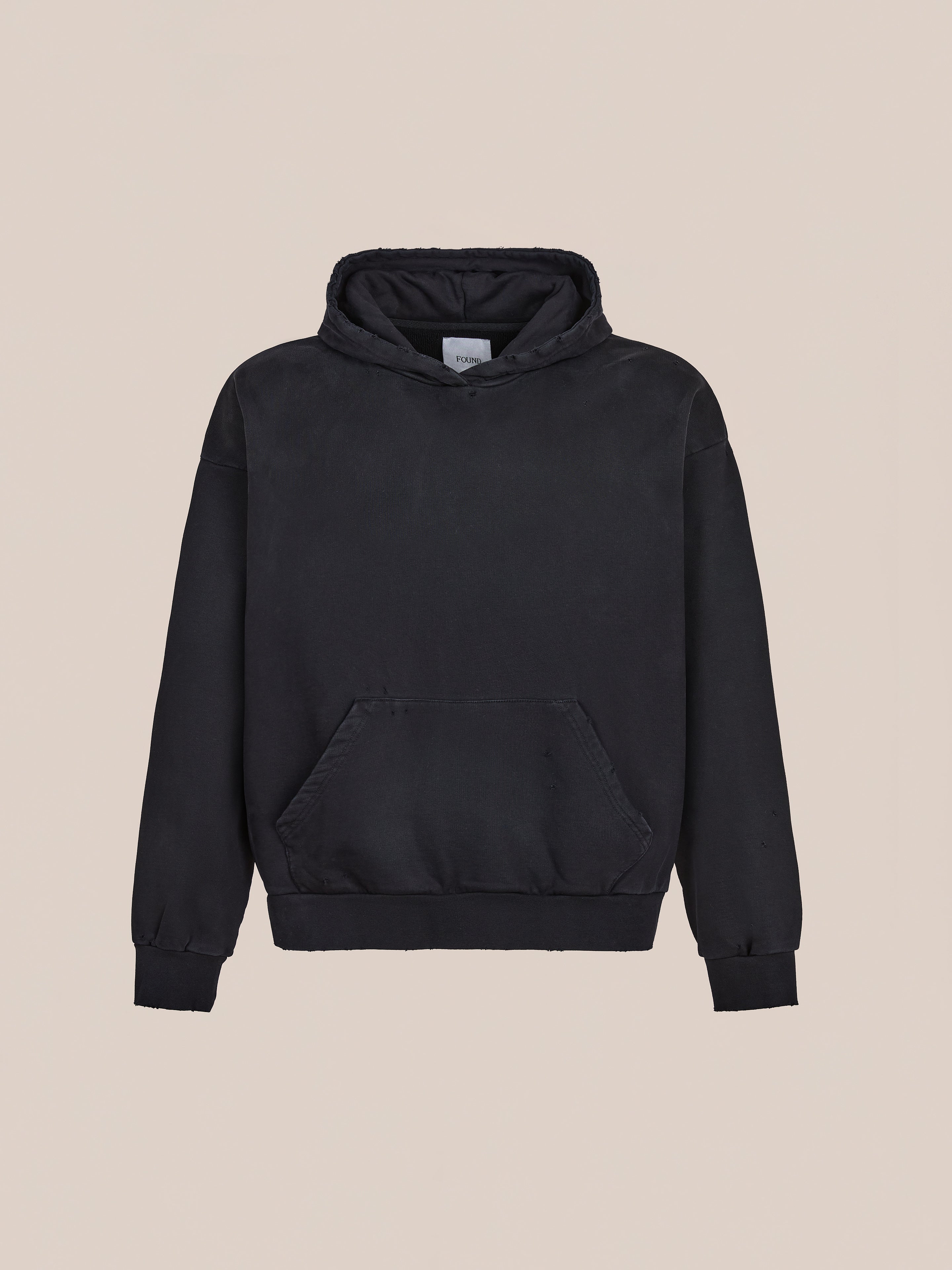 FOUND Distressed Pullover Hoodie in vintage black, unisex relaxed fit with front pocket and ribbed cuffs, shown on a plain beige background.