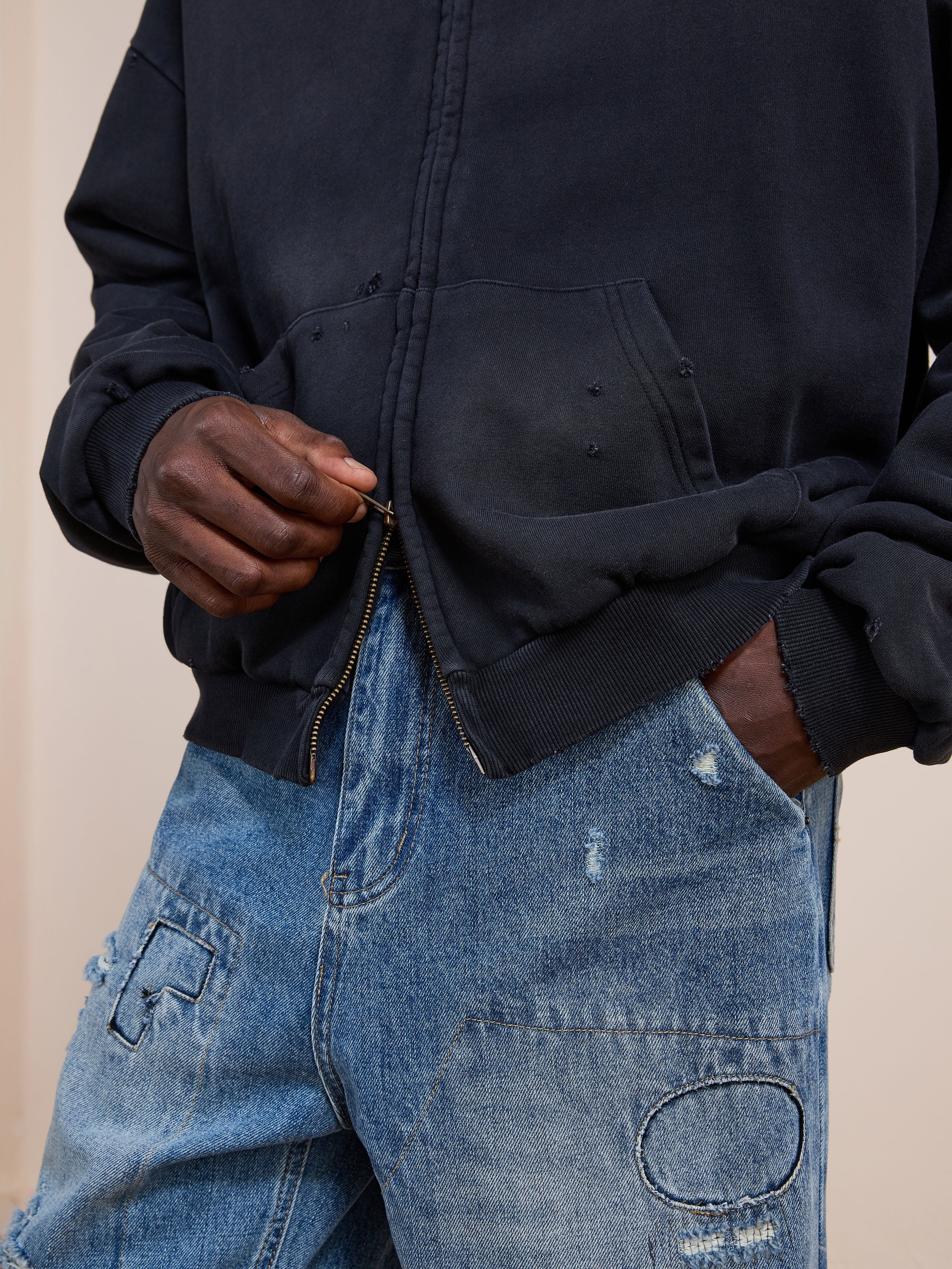 A person wearing the FOUND Distressed Thermal Lined Zip Up Hoodie and distressed blue jeans with patchwork detail holds the hoodie zipper.