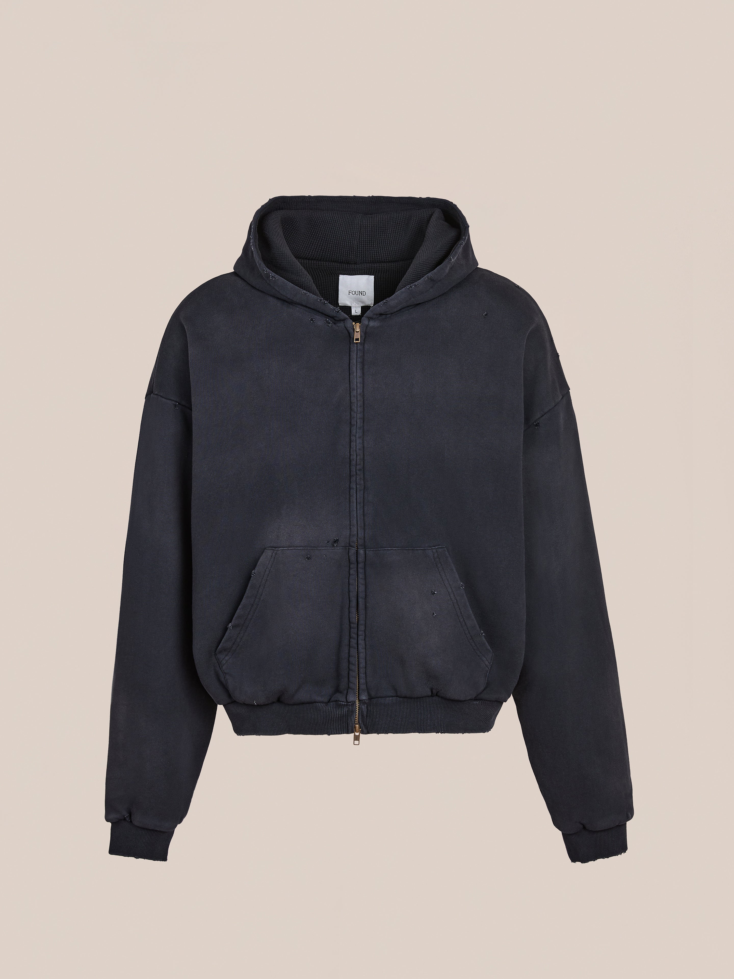 The FOUND Distressed Thermal Lined Zip Up Hoodie is a black unisex relaxed-fit hoodie featuring a hood, front pouch pockets, and ribbed cuffs and hem, shown against a plain beige background.