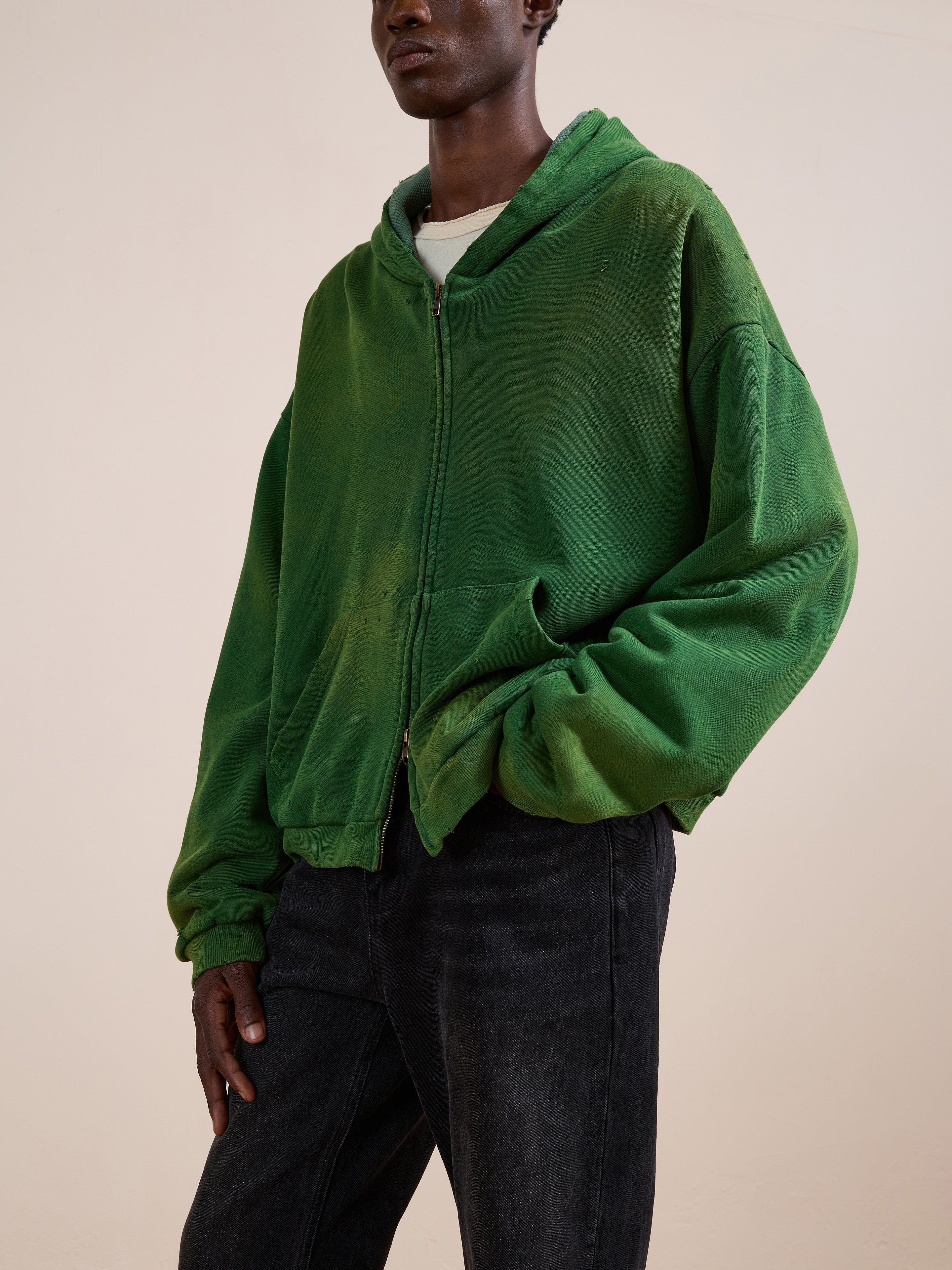 A model wears the FOUND Distressed Thermal Lined Zip Up Hoodie in green over a white shirt and black jeans, standing against a plain beige background.