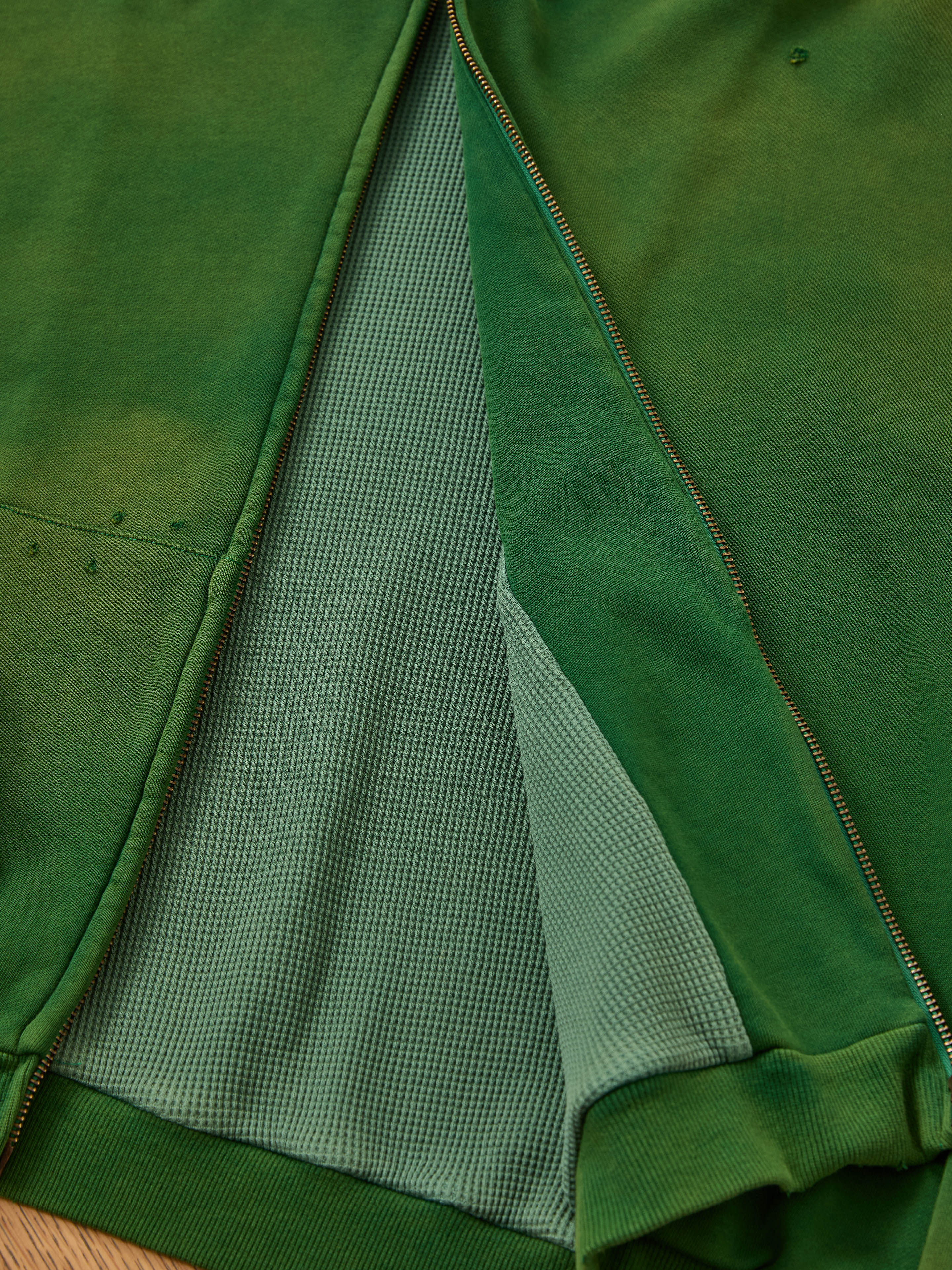 A close-up of the FOUND Distressed Thermal Lined Zip Up Hoodie in green, partially unzipped to show its textured, lighter green inner lining.