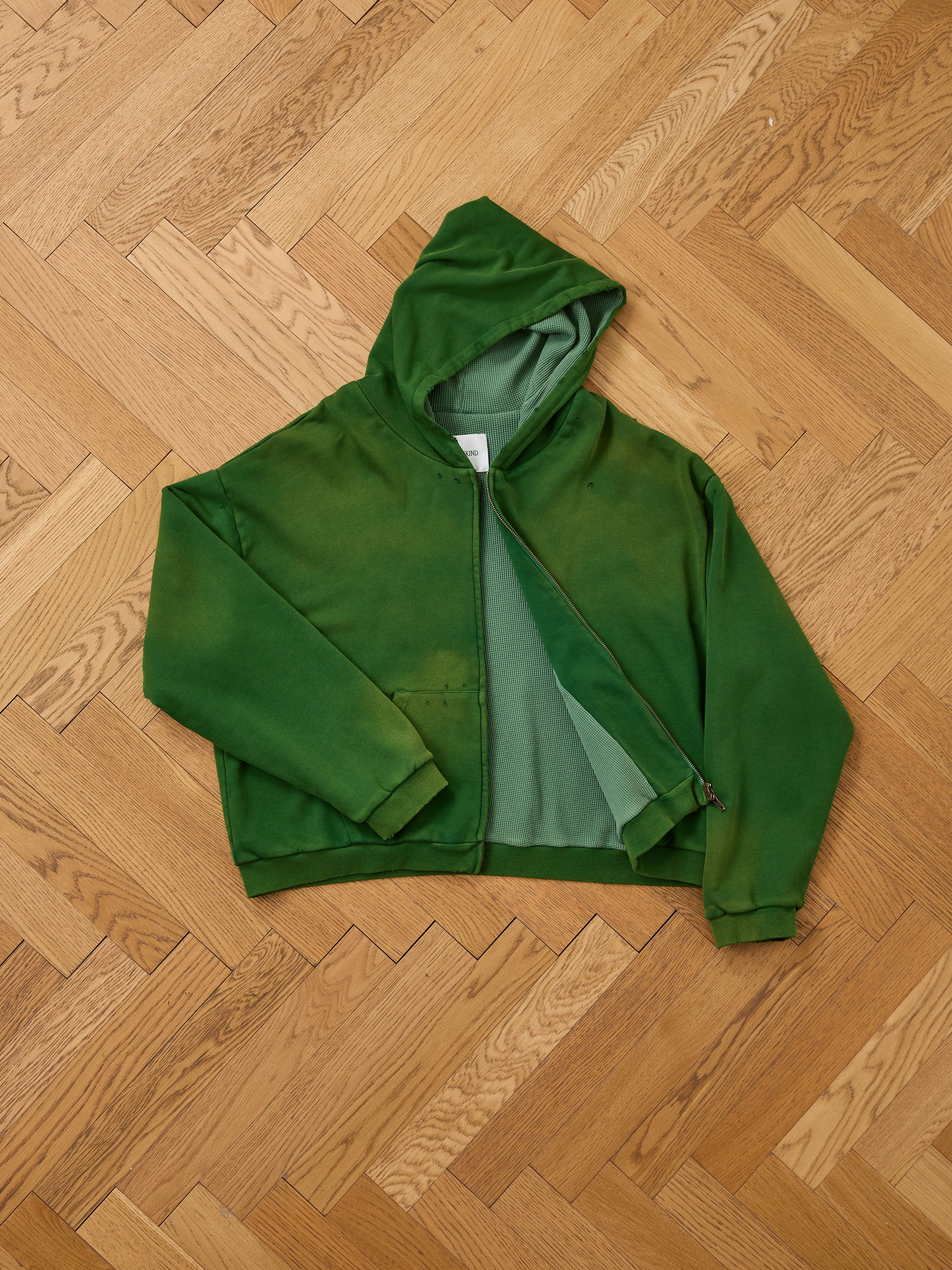 The FOUND Distressed Thermal Lined Zip Up Hoodie, featuring a cozy hood and partially unzipped style, is displayed flat on a wooden herringbone floor—ideal for warmth and laid-back style.