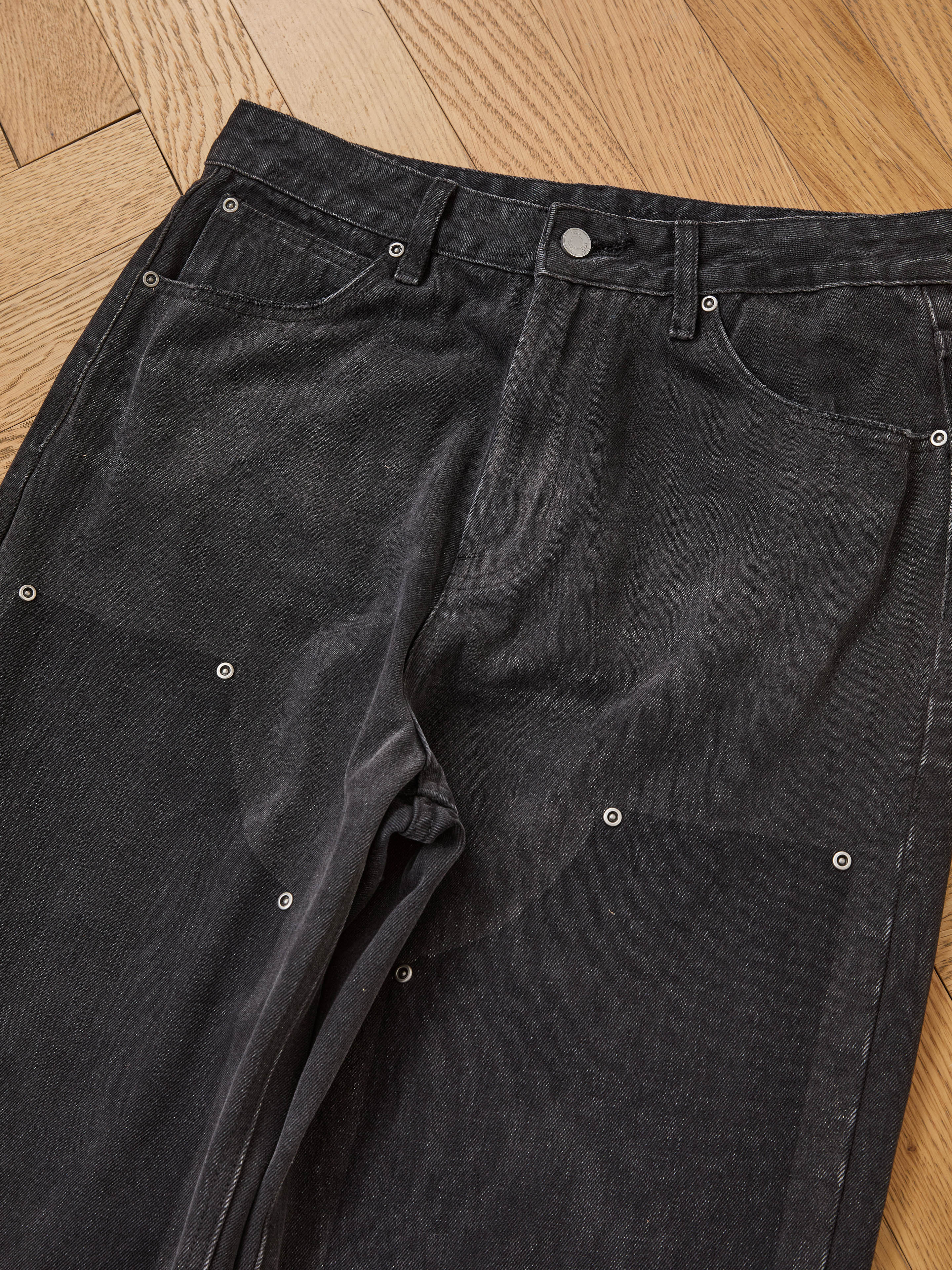 FOUND Double Knee Carpenter Jeans in a black vintage wash, featuring silver rivet details and a relaxed fit, shown lying flat on a wooden floor.