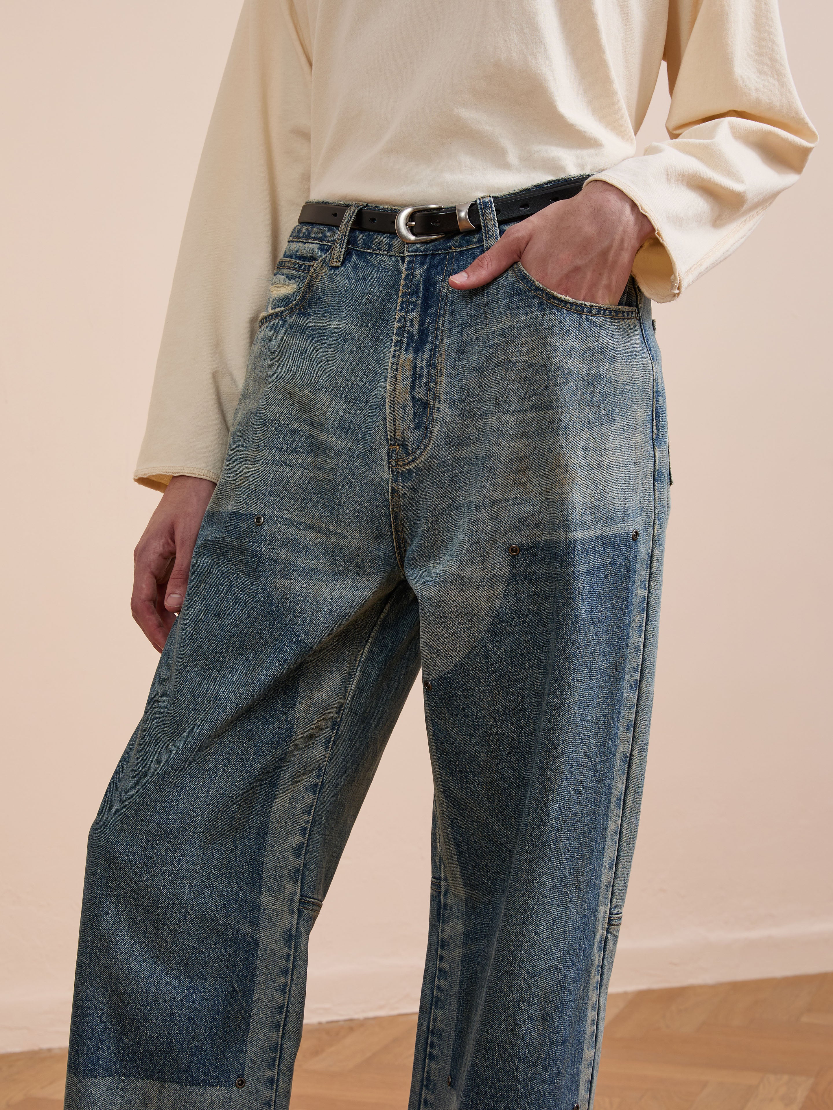 A person wears FOUND Double Knee Carpenter Jeans, a light long-sleeve shirt, and a black belt, with one hand in their pocket.