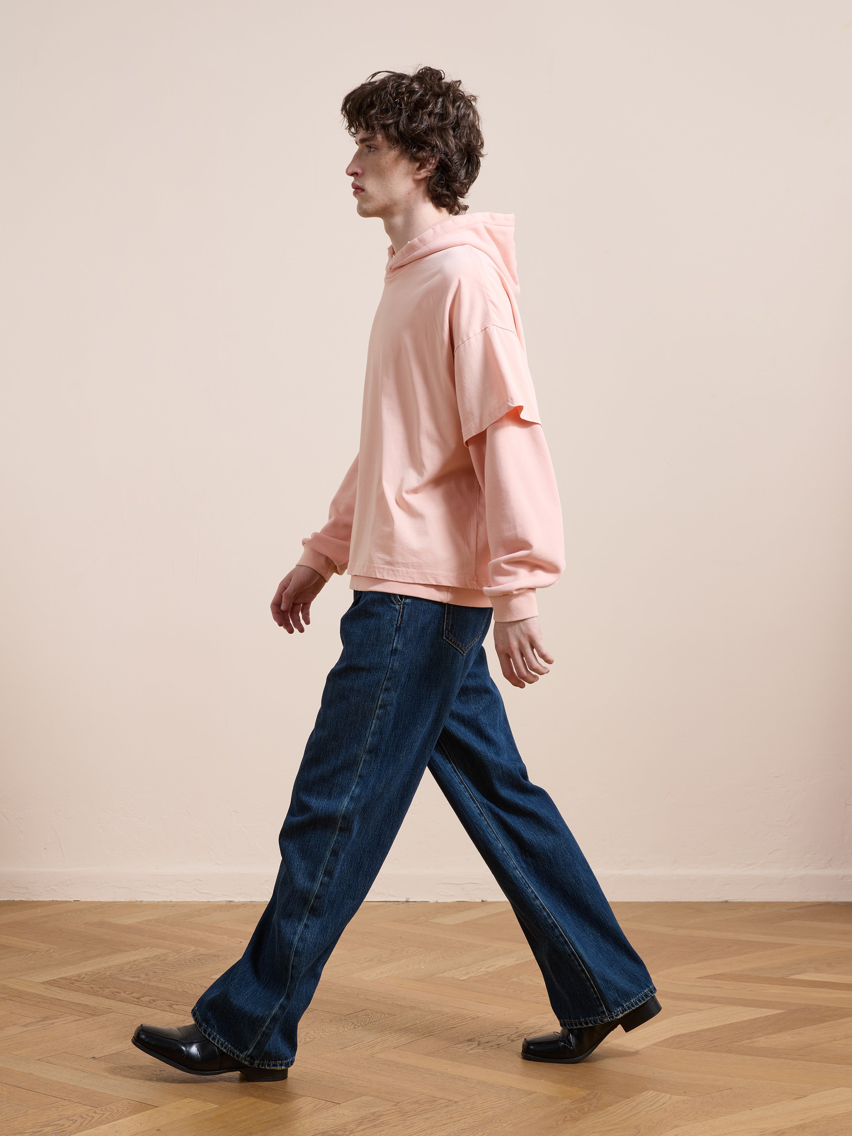 Someone wearing the Found Double Layer Hoodie and wide-leg blue jeans walks indoors on a wooden floor, facing left.