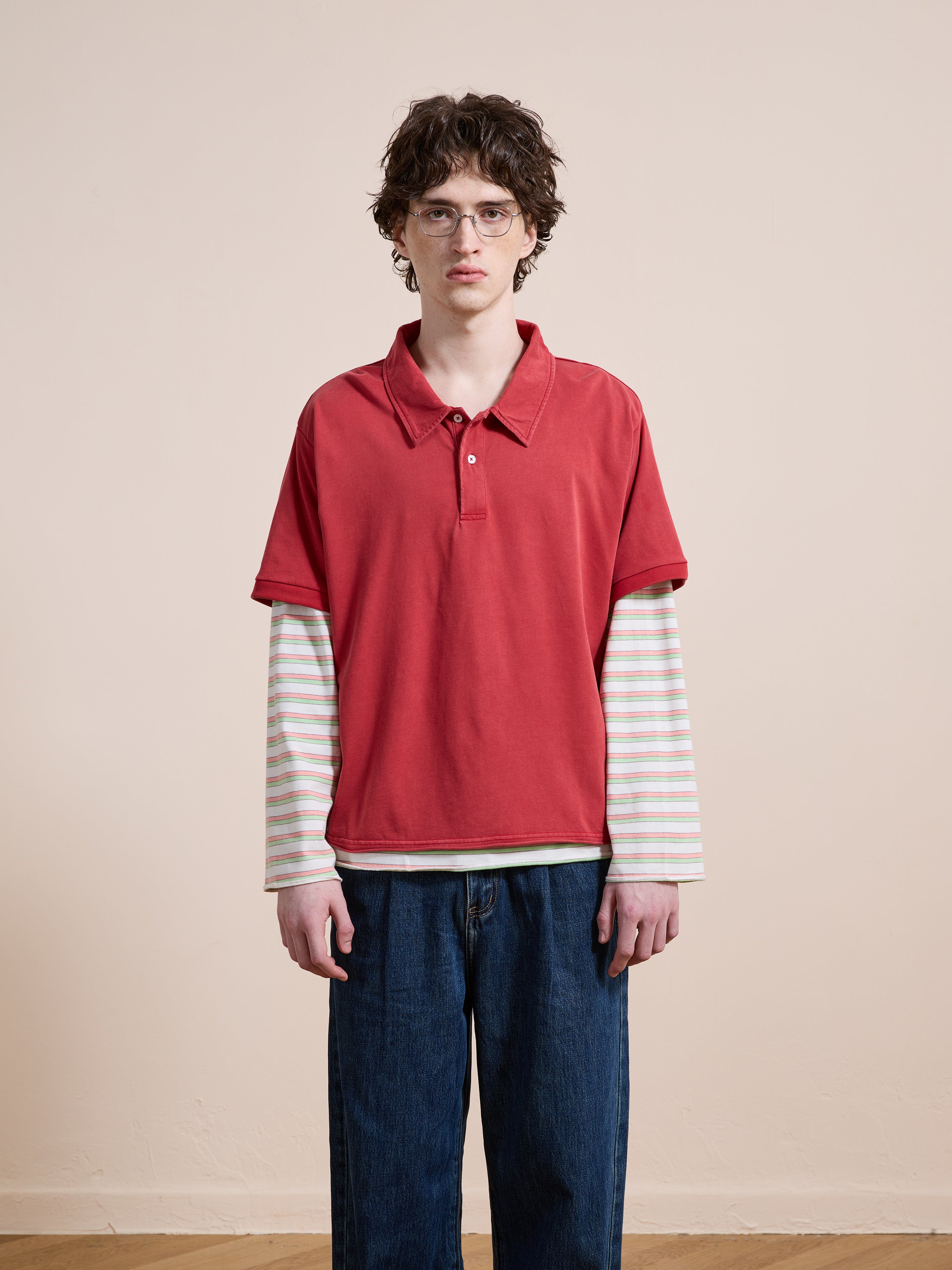 A person with short curly hair and glasses wears the FOUND Double Layer Stripe Polo with blue jeans, standing against a plain beige background.