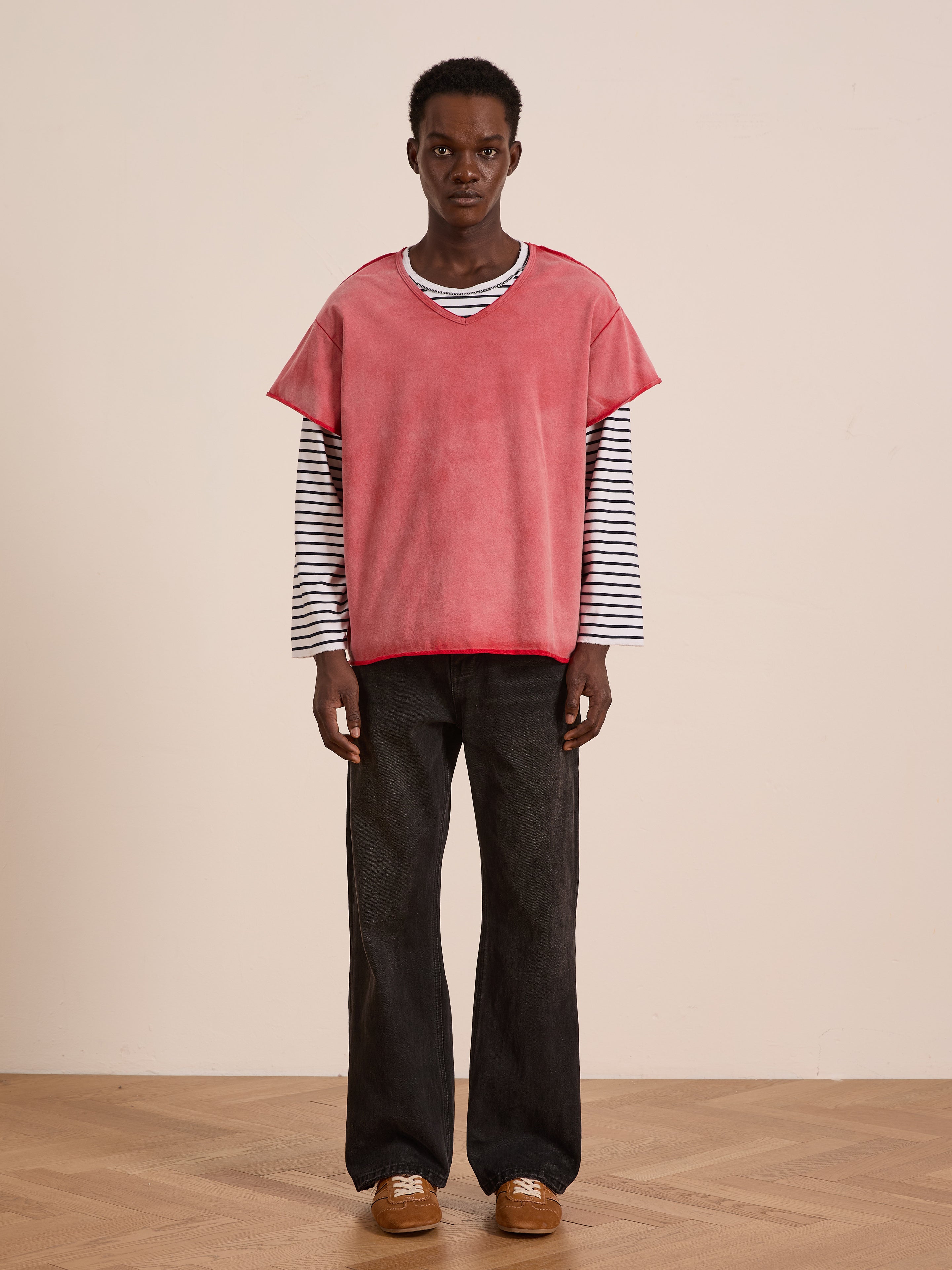 Indoors, someone models easy layering with a pink short-sleeve top over the FOUND Double Layer LS Tee, paired with loose black pants and brown shoes on a wooden floor.