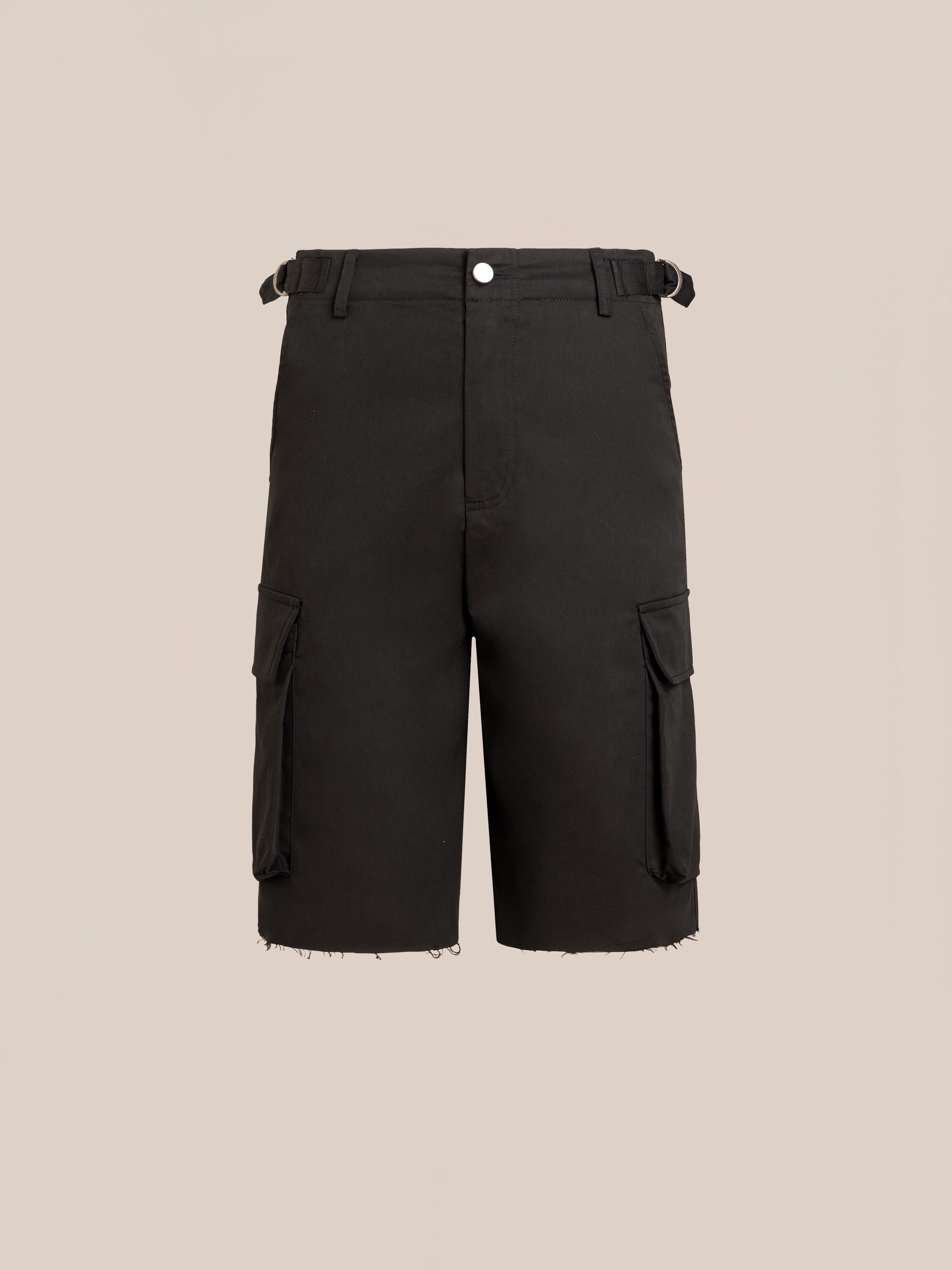 Found Elbas Cargo Shorts in black feature dual cargo pockets, belt loops, front button closure, side pockets, adjustable waist tabs, and raw-edged hems on a plain beige background.