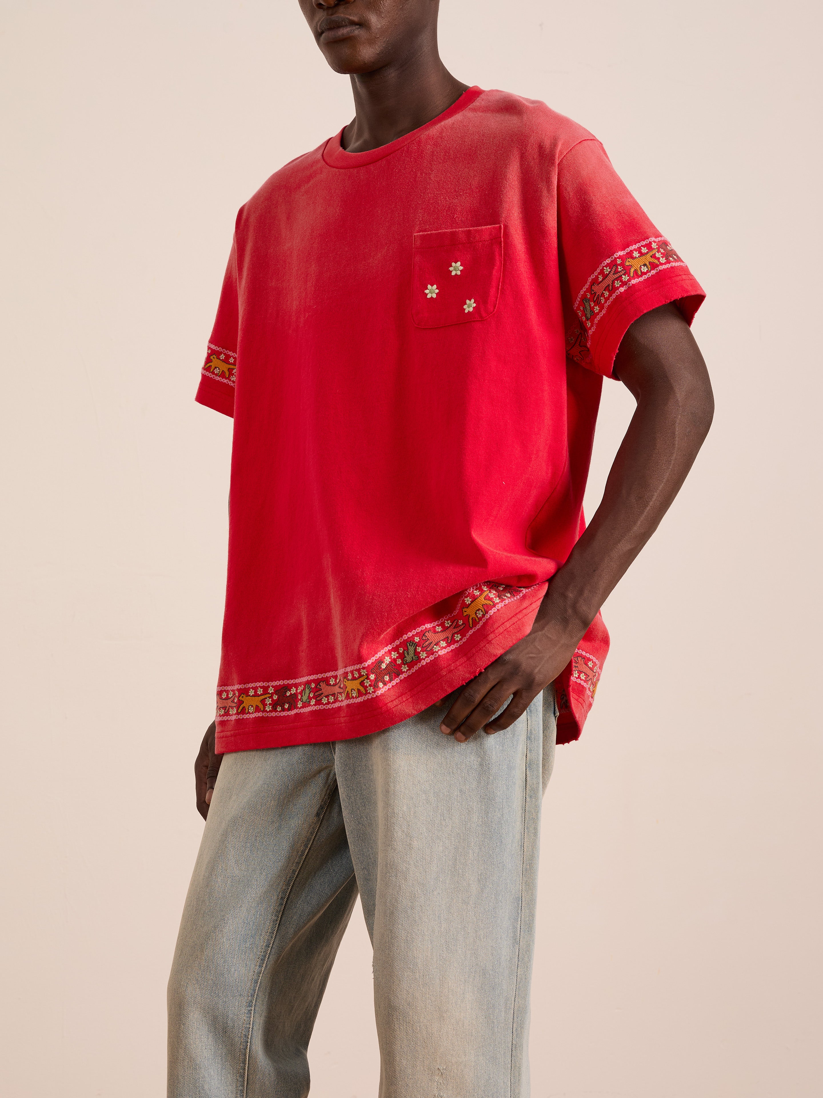 A person wears the FOUND Horse Motif Embroidered Tee, featuring a loose fit, vintage wash, and decorative trim on the sleeves and hem, paired with light blue jeans against a plain background.
