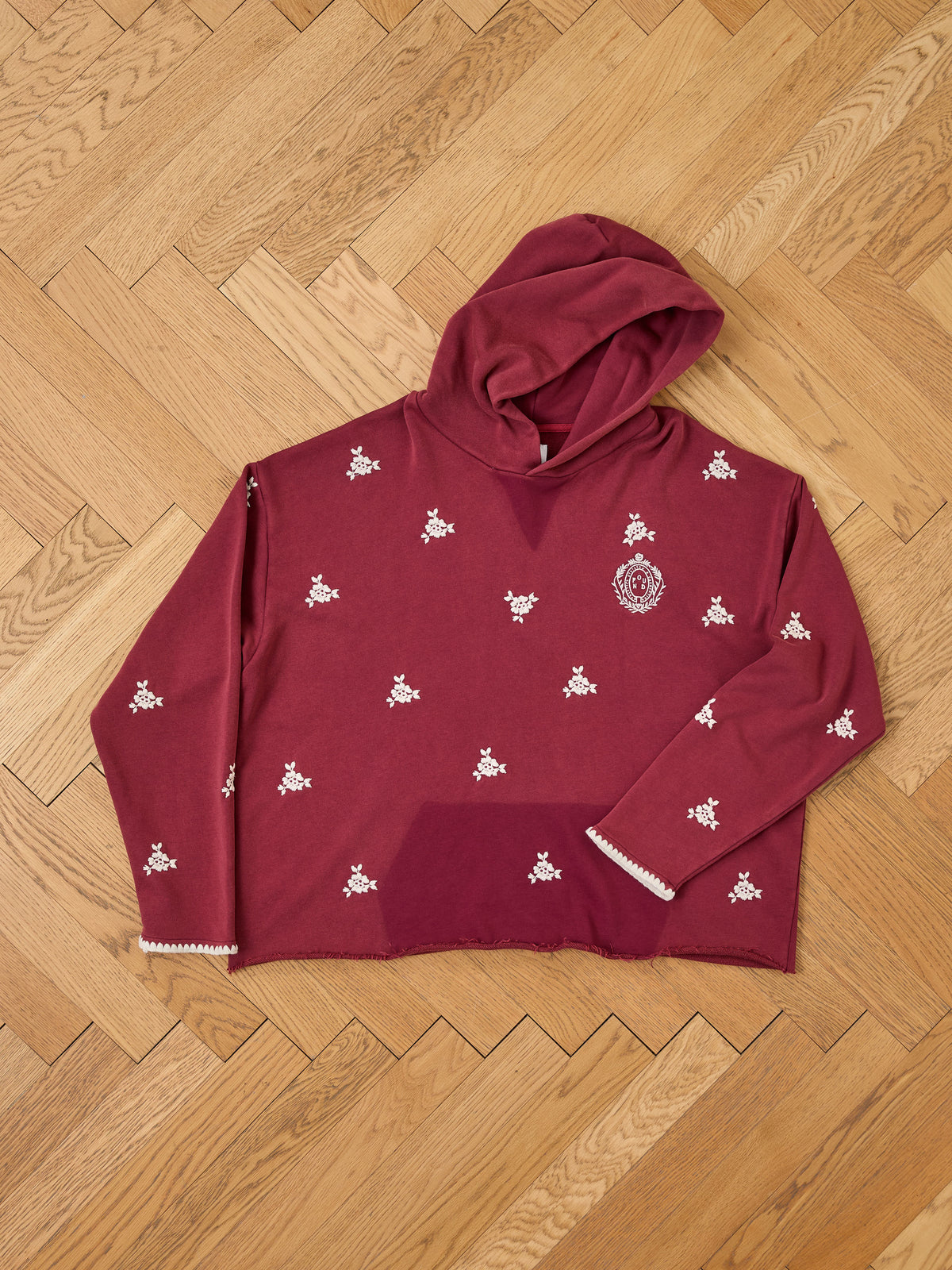 FOUND Embroidered Motif Hoodie in maroon with white floral embroidery, unisex relaxed fit, shown flat on a wooden herringbone floor.