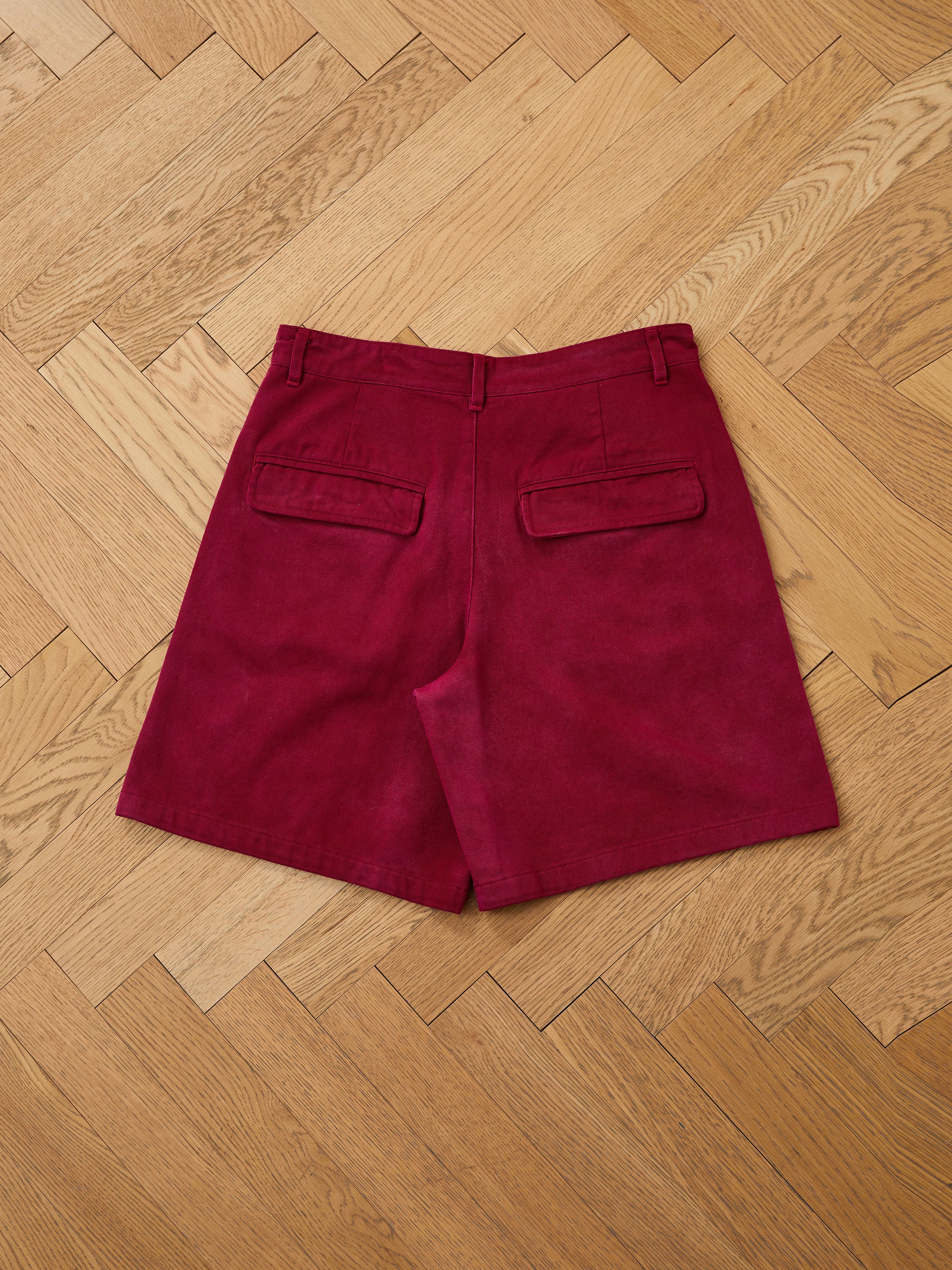 Found Embroidered Duck Shorts in vintage maroon, featuring back pockets and belt loops, shown laid flat on a wooden herringbone floor.