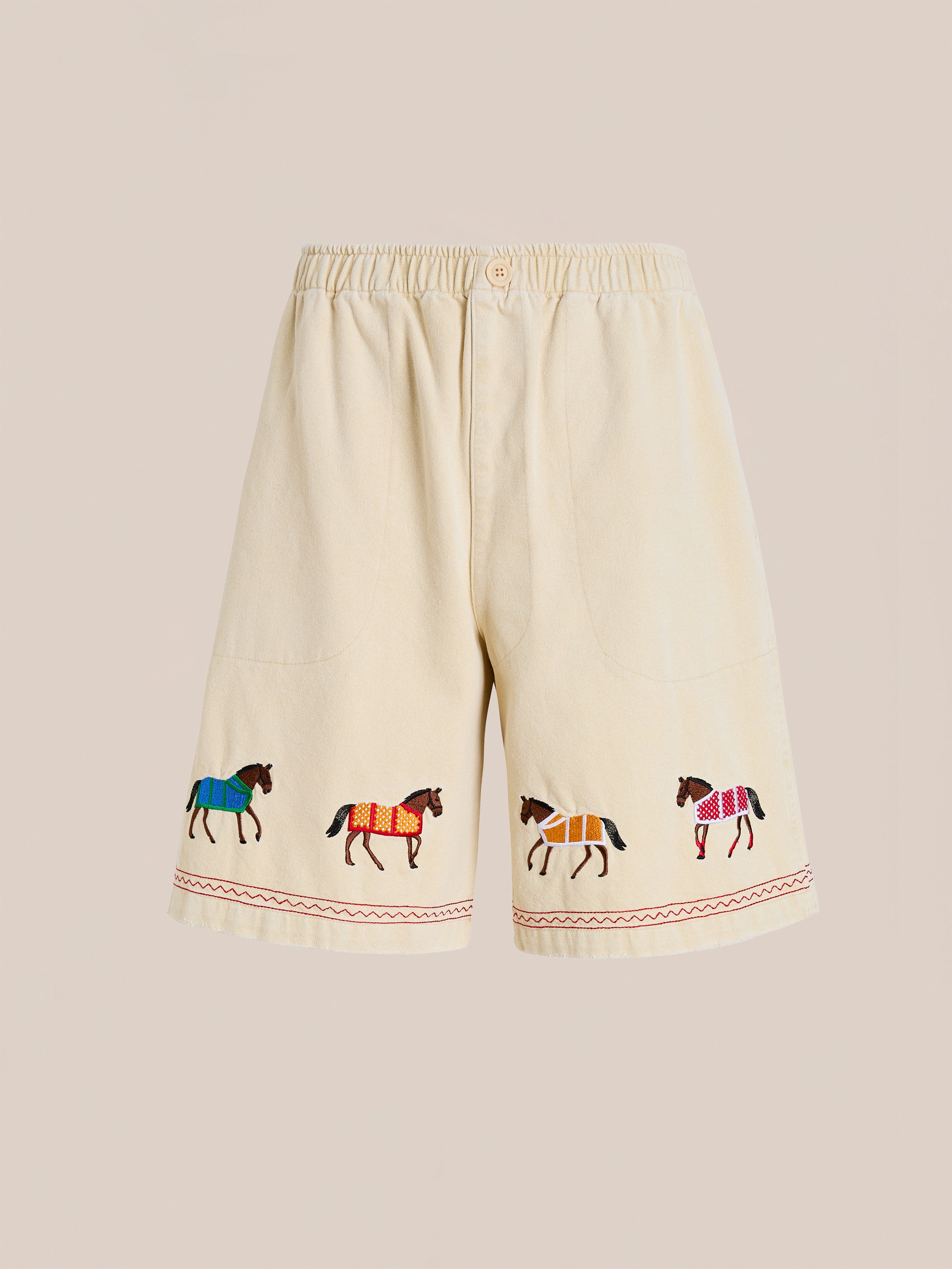 The Profound Embroidered Horse Shorts are beige cotton twill shorts with an elastic waistband, front pockets, and colorful embroidered horses along the hem.