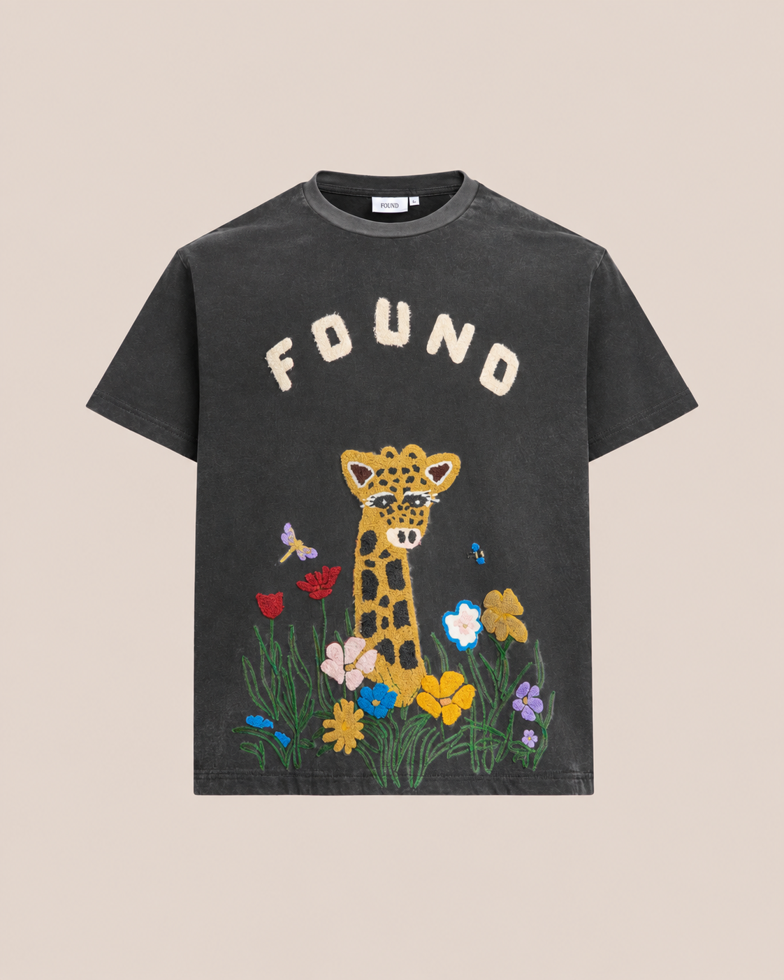 The FOUND Embroidered Wildlife Tee features “FOUND” above a chenille giraffe, with colorful flowers, grass, and butterflies—a bold nature-inspired design.