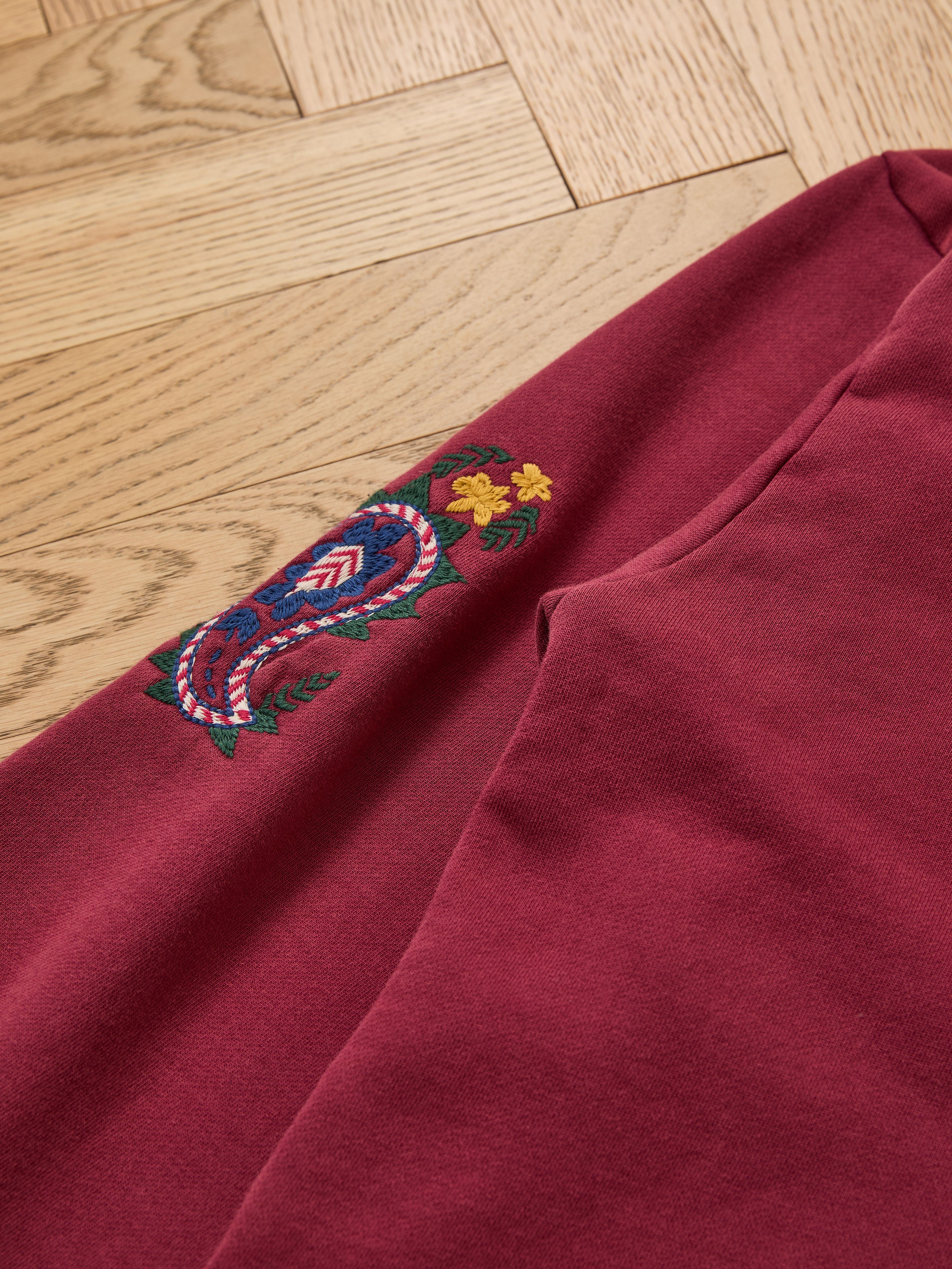 Close-up of the FOUND Embroidered Kantha Paisley Hoodie in maroon, showcasing Kantha-inspired paisley and floral embroidery, laid on a light wood herringbone floor.