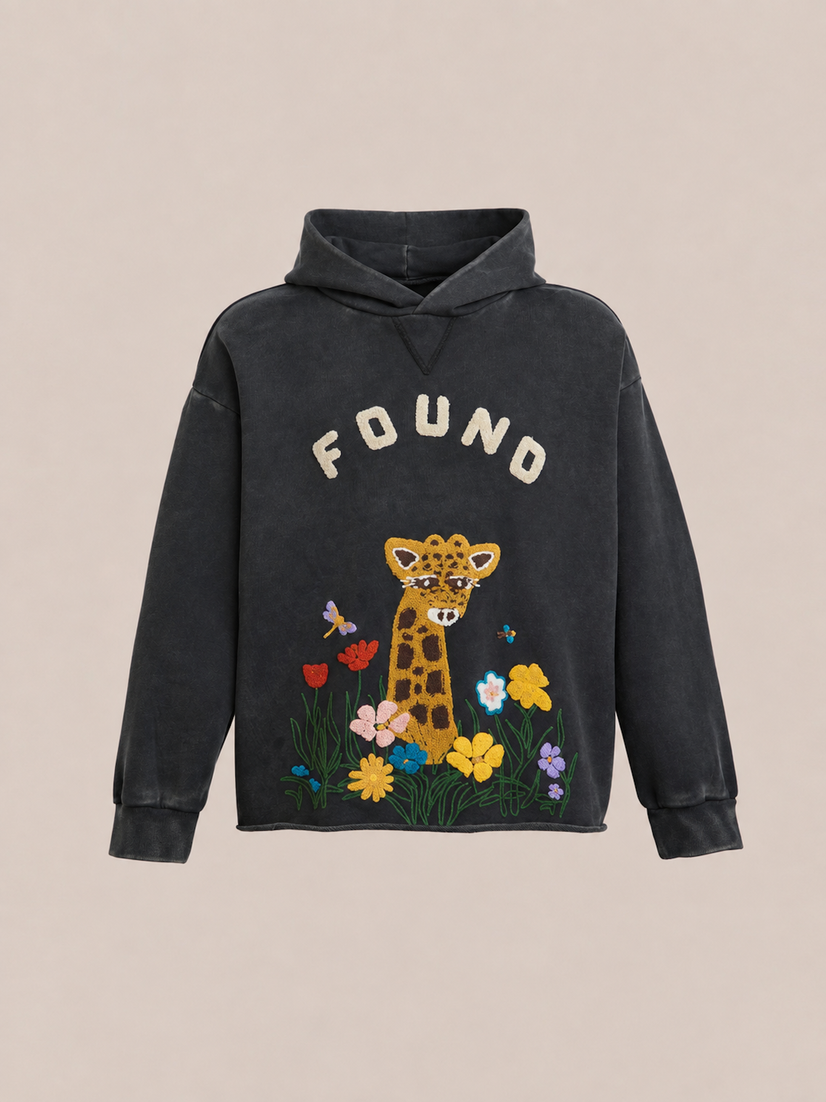 The Embroidered Wildlife Hoodie by FOUND features “FOUND” text above an embroidered giraffe and colorful flowers on the front, crafted from vintage French-terry cotton and shown against a beige background.