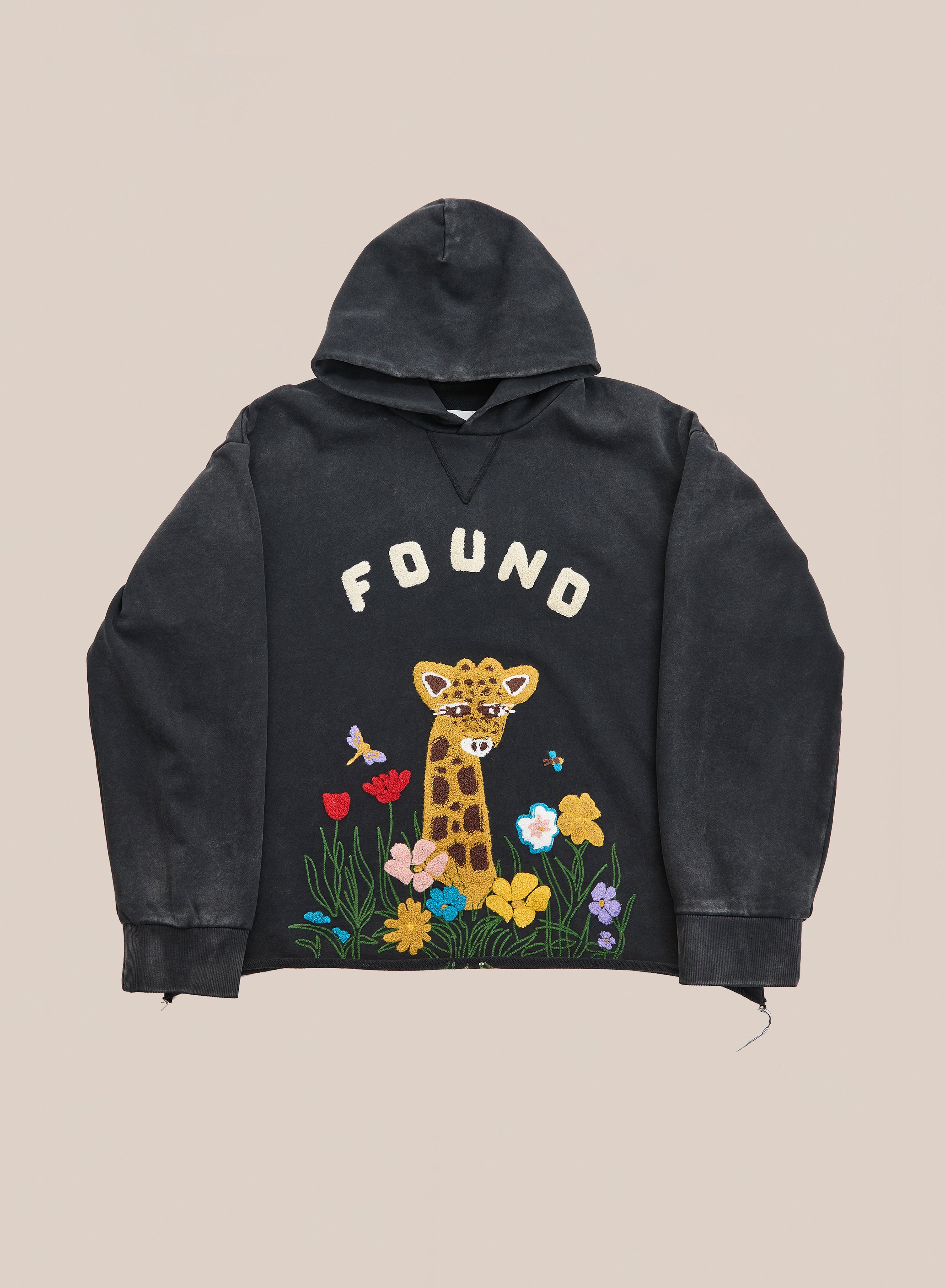 Discover the Embroidered Wildlife Hoodie by FOUND—an elegant black hoodie featuring beautifully embroidered cartoon giraffe, flowers, and butterflies with signature “FOUND” text on the front. Crafted from vintage French-terry cotton, this hoodie effortlessly blends comfort and style, making it a playful addition to your wardrobe.