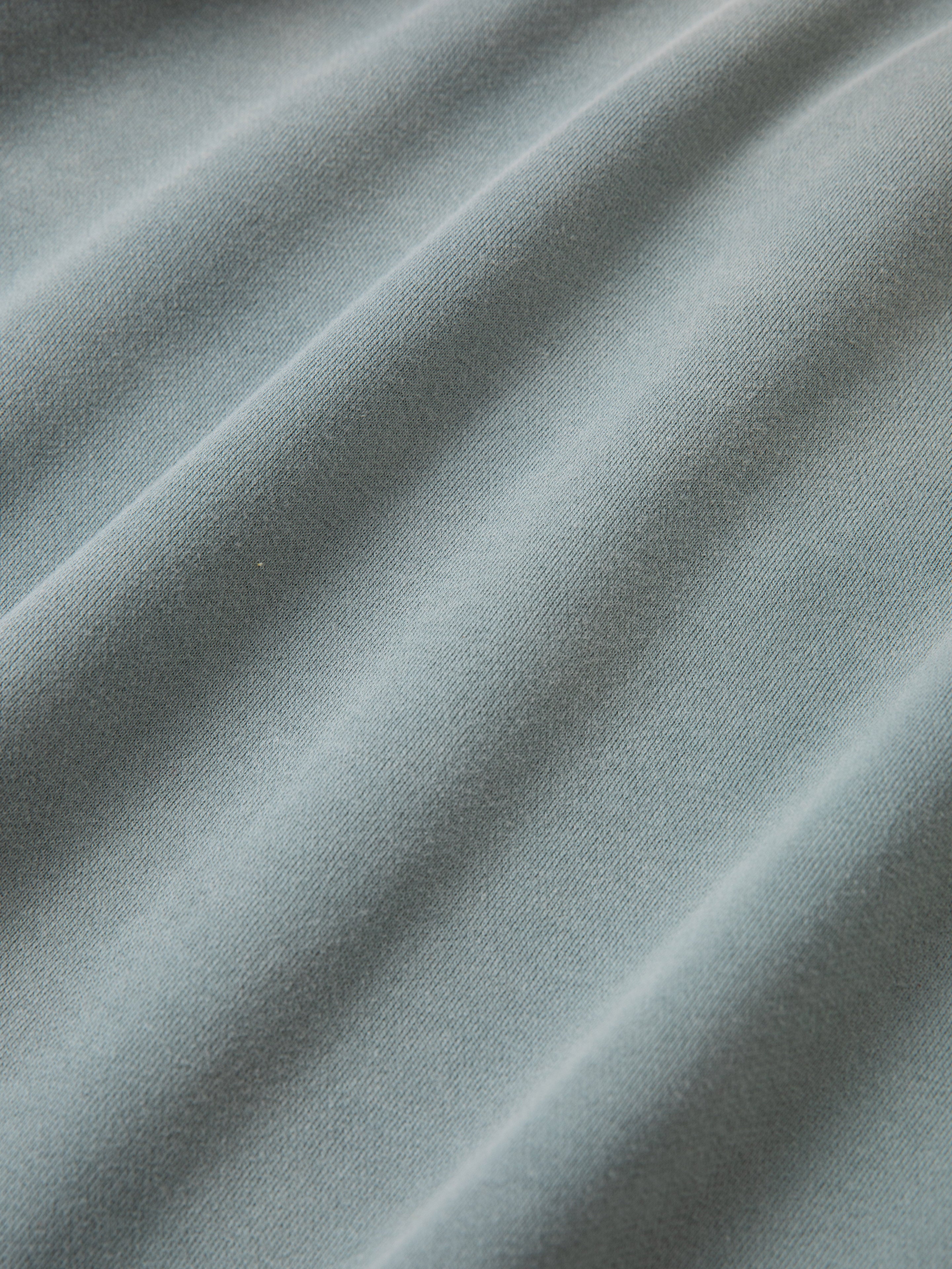 Close-up of light blue French Terry cotton fabric with a soft texture and visible folds. The fabric appears smooth, and the light highlights its gentle draping, bringing a vintage-inspired charm to the Multi Patch Hoodie by FOUND.