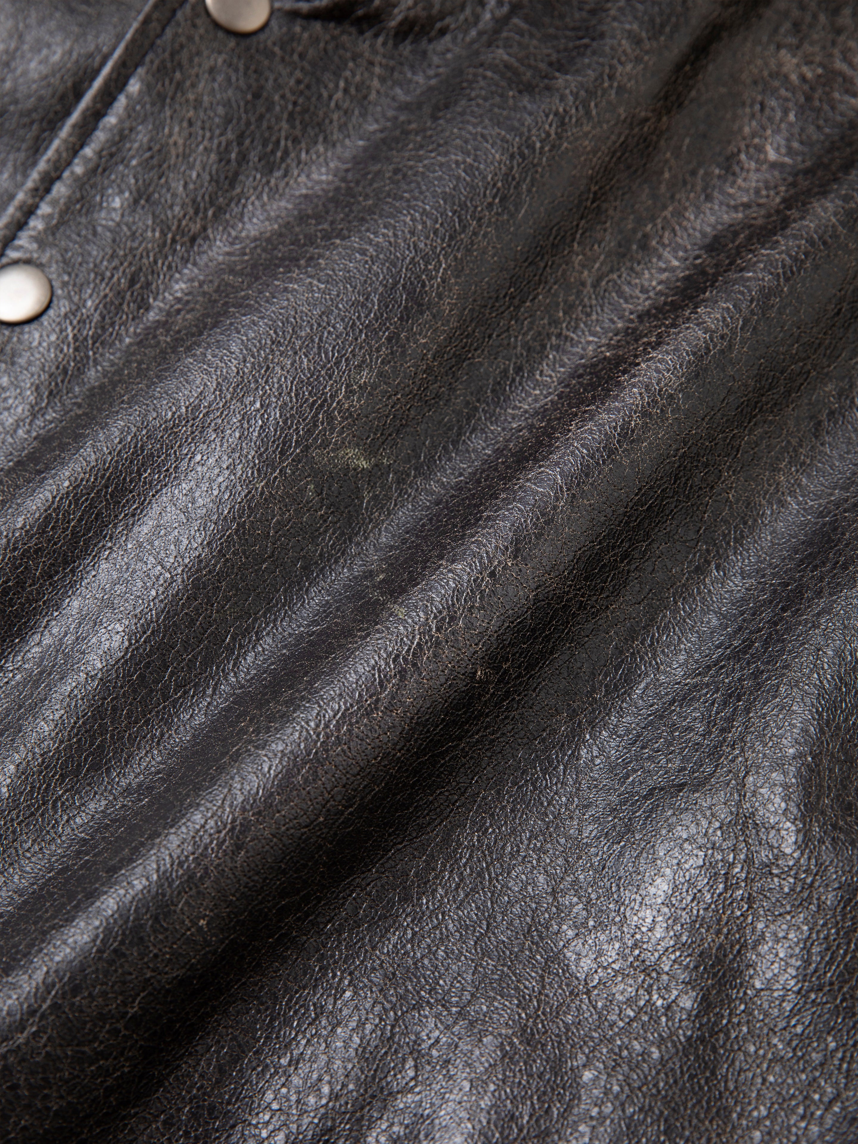 Close-up of a distressed genuine leather hoodie by Found, showcasing its rich texture and grain, crafted from ethically sourced materials, with visible side buttons.