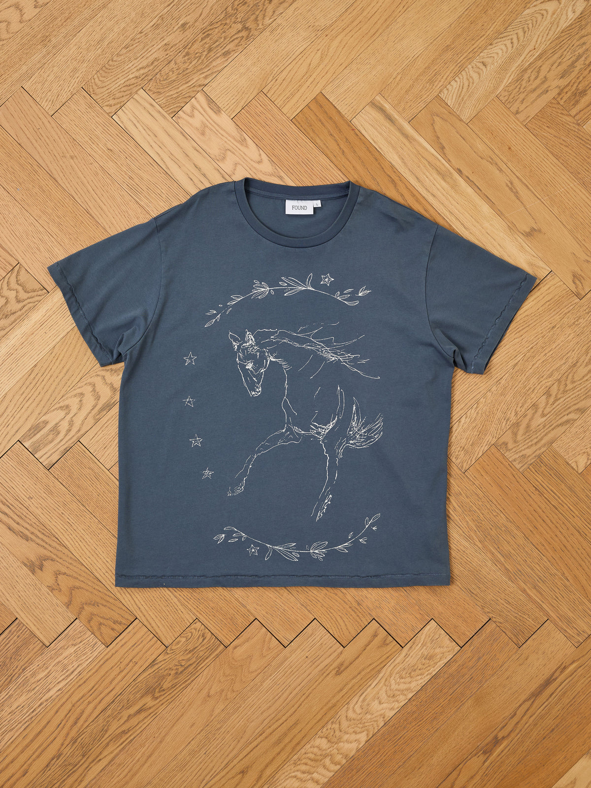The Faded Horse Trot Tee by FOUND is a unisex relaxed fit with outlined horse, stars, and branches on dark gray—perfect for equestrian style.