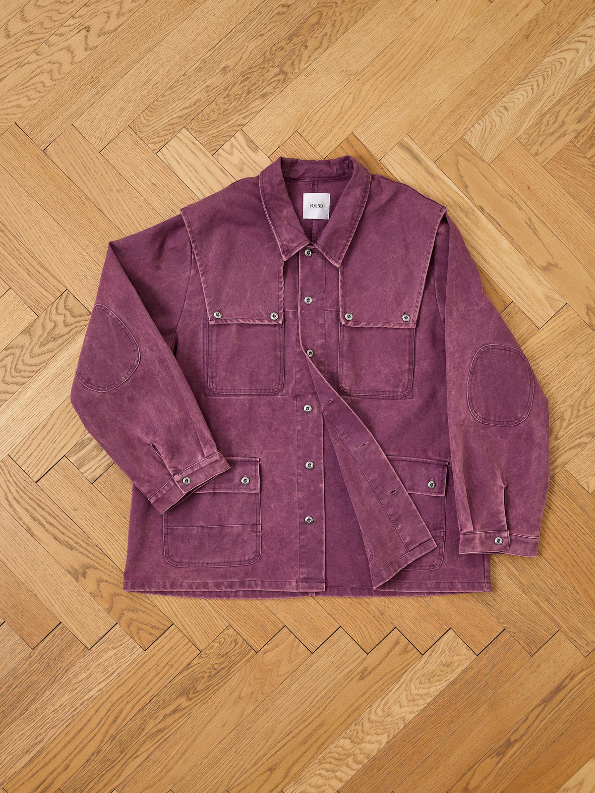 The Found Faded Paneled Cargo Jacket, featuring a purple corduroy design with four front pockets and button closures in a classic utility outerwear style, is laid flat on a light wood herringbone floor.