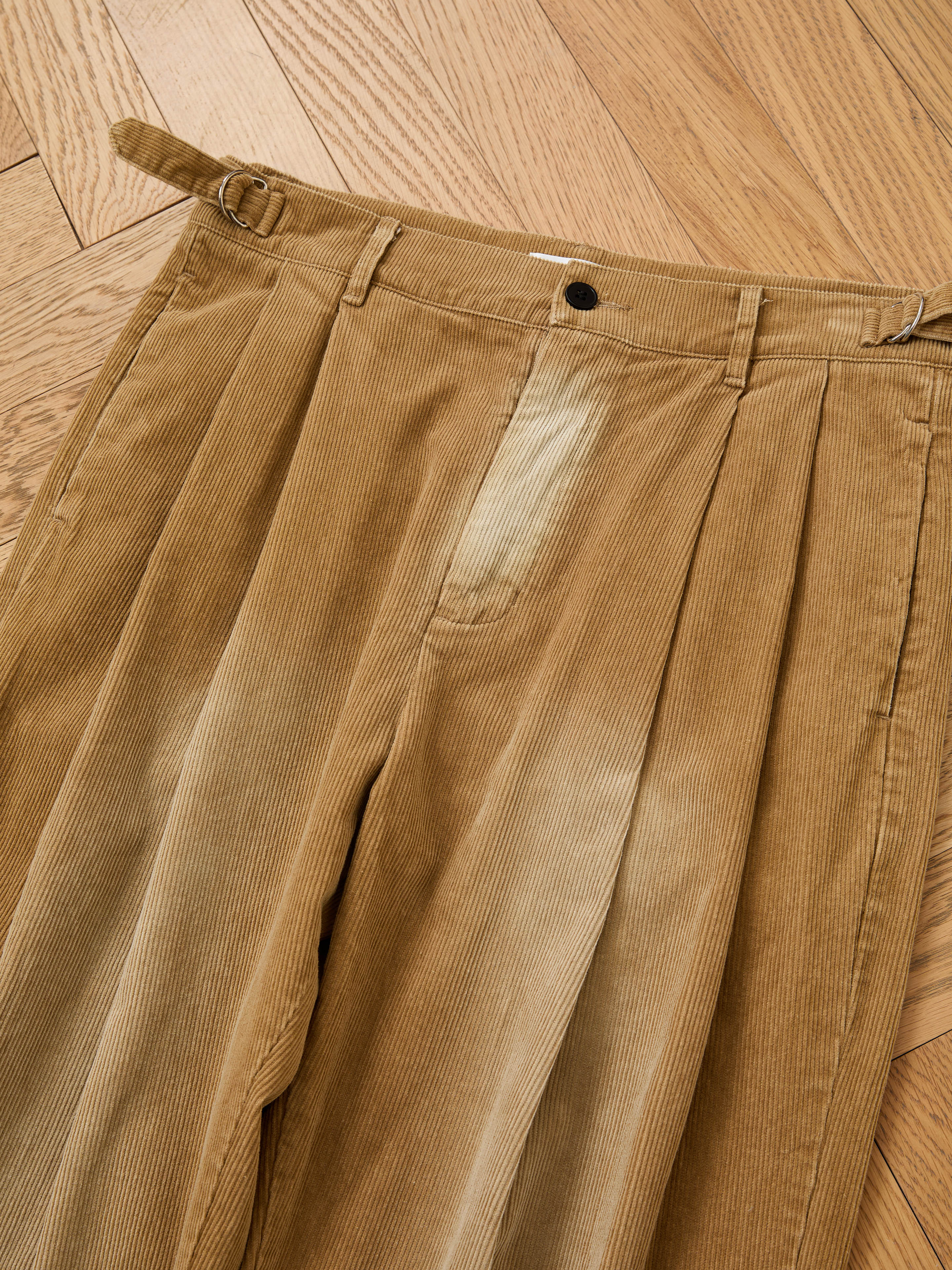 FOUND Faded Pleated Corduroy Pants in tan, relaxed fit with front discoloration, shown laid flat on a wooden floor.