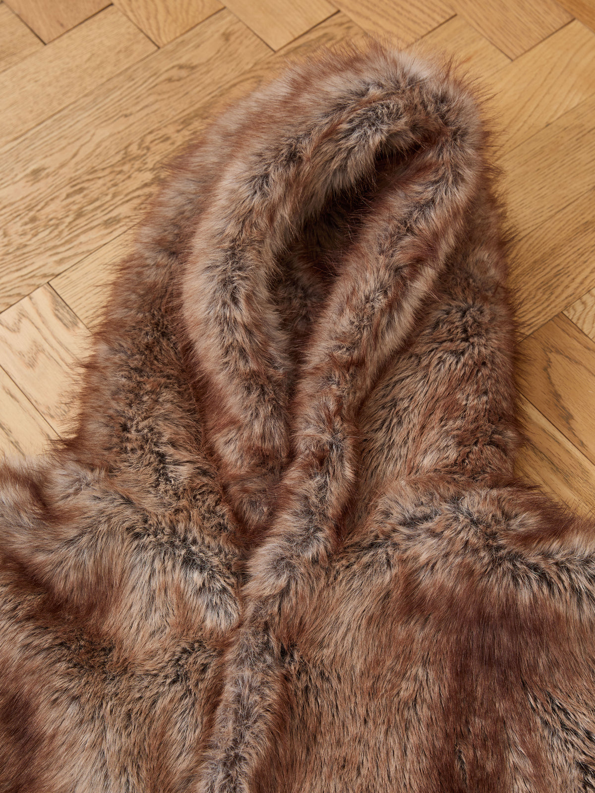 FOUND Faux Fur Hoodie in brown faux fur, shown laid flat on a wooden parquet floor—ideal as cozy vintage-inspired outerwear or a unisex winter jacket.