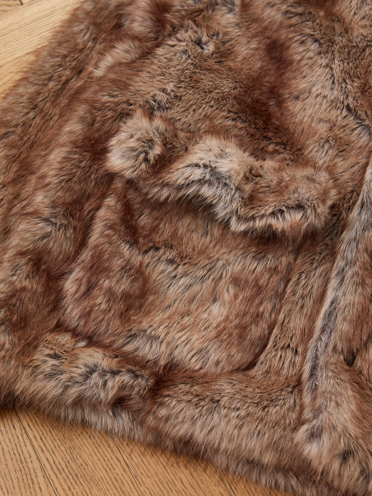 A close-up of the FOUND Faux Fur Hoodie on a wooden floor, displaying its soft texture and natural brown color variations.