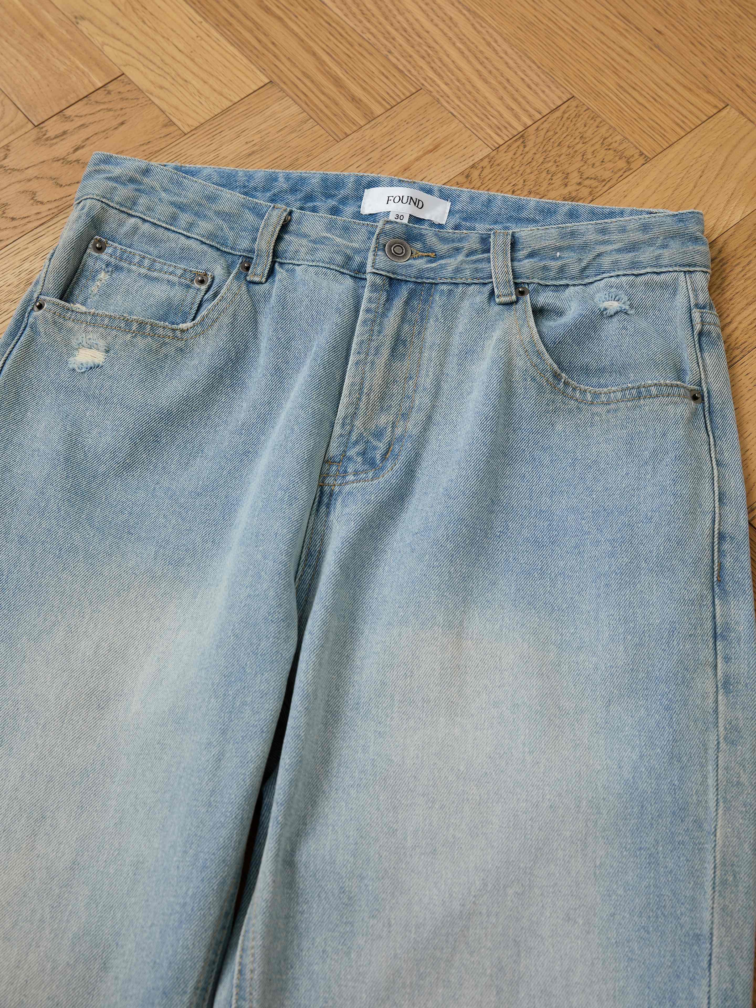 Found Flare Jeans in light blue denim feature subtle distressing and distressed hems, shown laid out on a wooden floor.