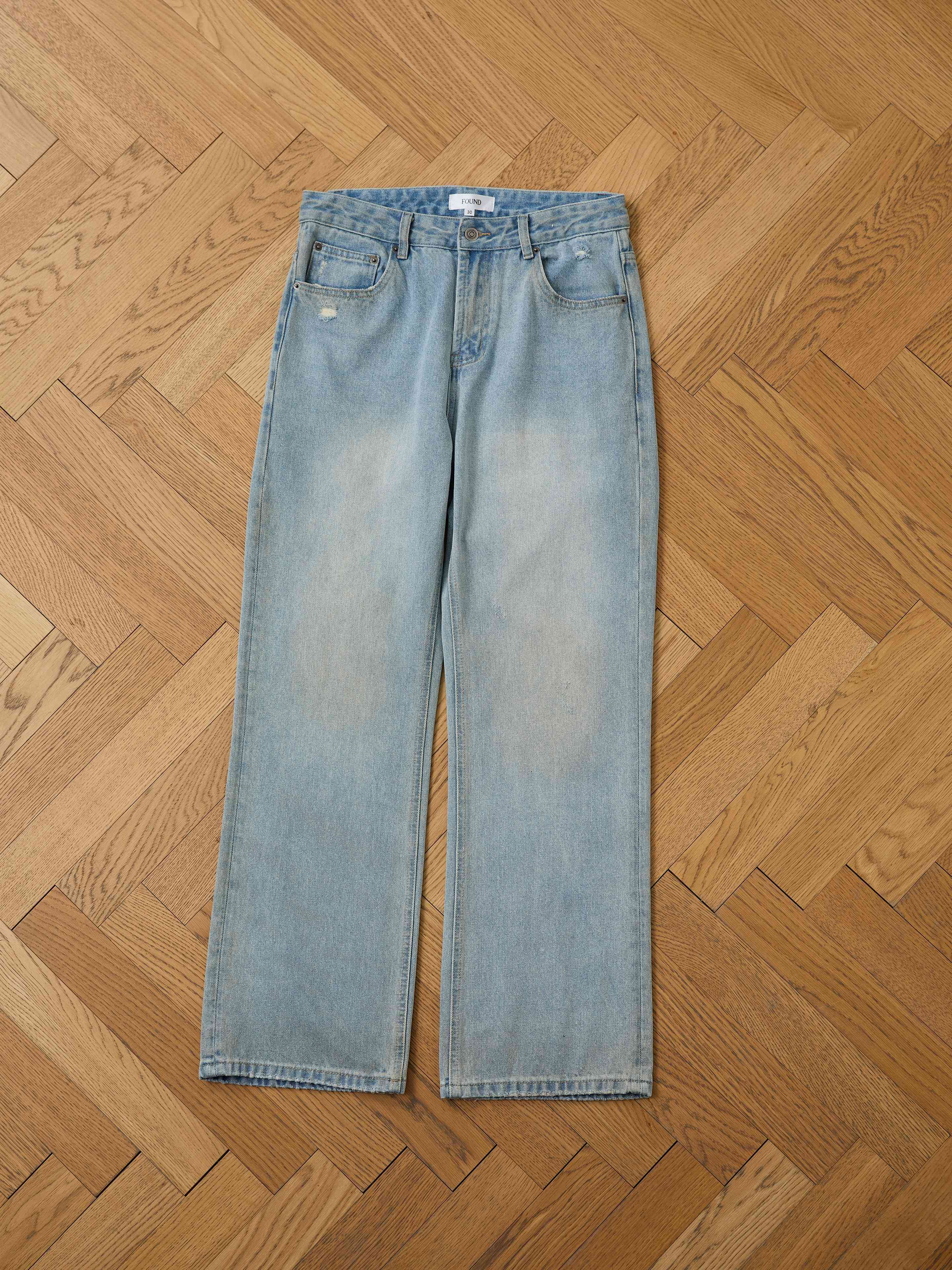 A pair of Found Flare Jeans in light blue denim is displayed flat on a light brown herringbone wood floor.